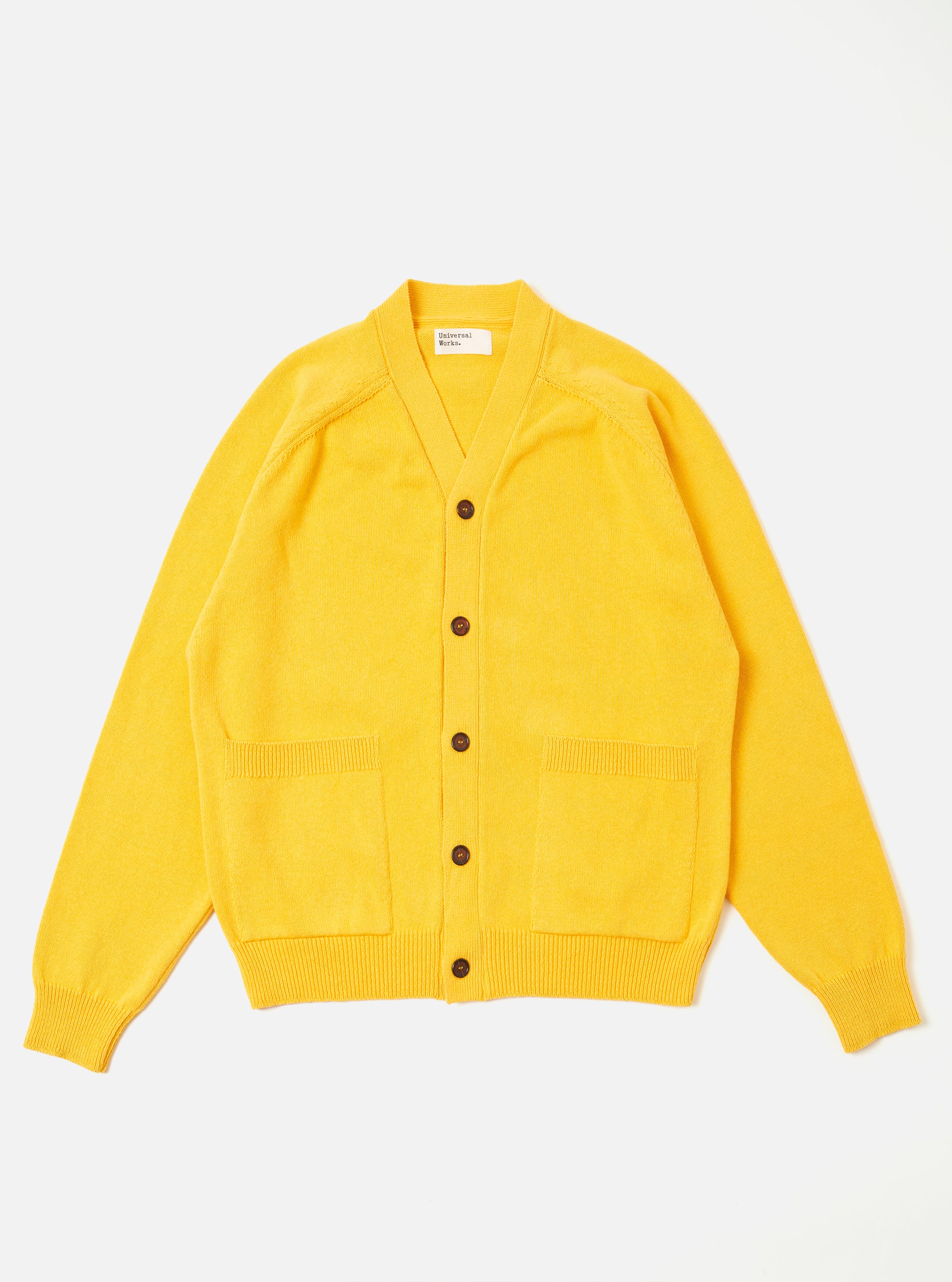The Yellow Eco Cotton Knit Pocket David Cardigan is shown as a flat lay against a white background. The cardigan features a V-neckline, a five-button front closure, and two large patch pockets at the waist. The knit fabric has a textured, ribbed appearance in a vibrant yellow ochre color with tonal binding along the edges.