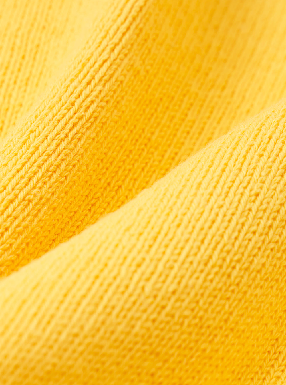A close-up fabric swatch of the Yellow Eco Cotton Knit Pocket David Cardigan highlights the vibrant yellow color and the detailed texture of the eco cotton knit material. The fabric fills the frame, providing a clear view of the garment's construction.