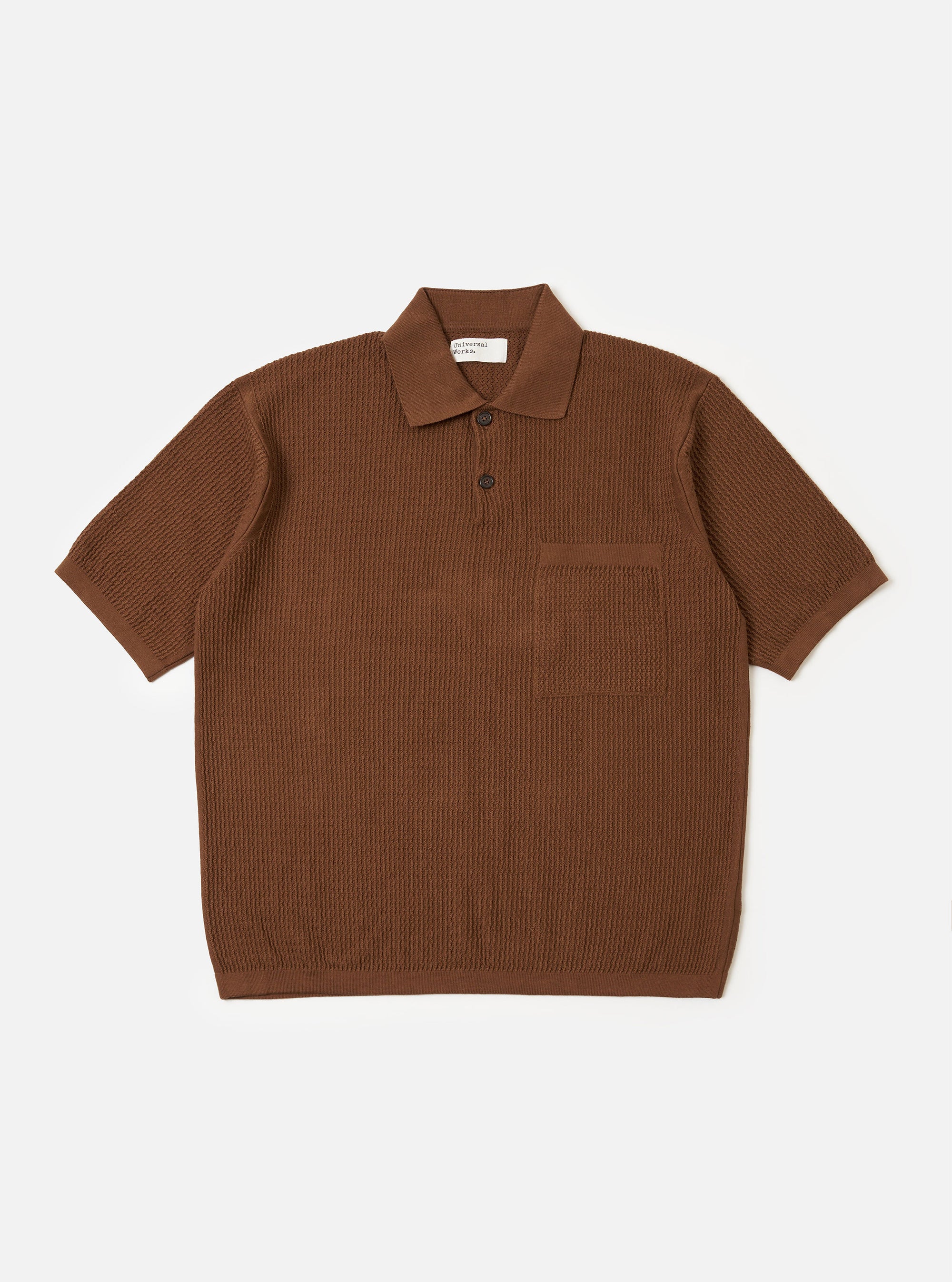 The Brown Fine Texture Tricot S/S Knit Polo is shown as a flat lay against a plain white background. The short-sleeved polo features a raised rib-patterned texture, a neat collar, a two-button placket, and a large square patch pocket on the left chest.