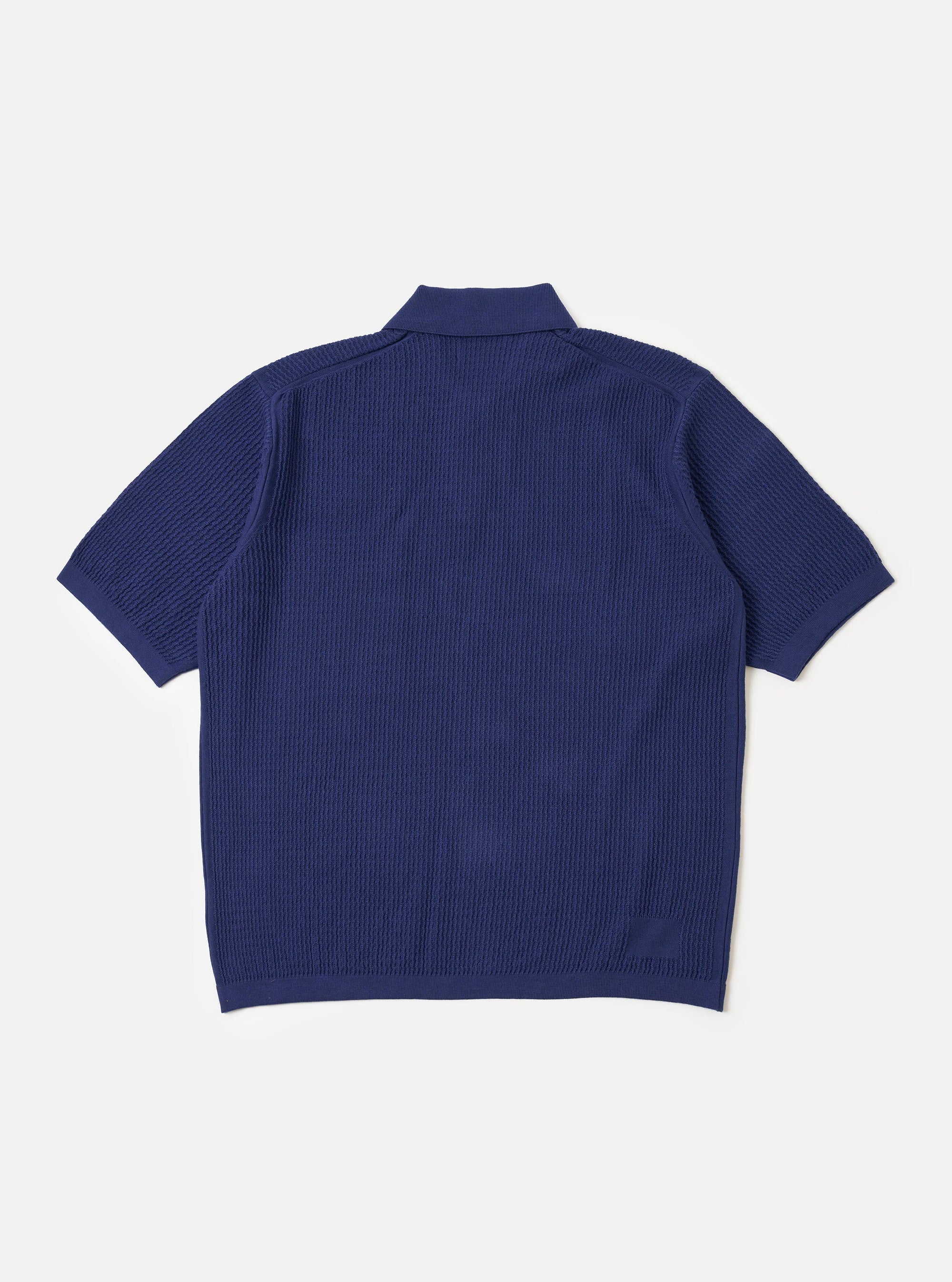 The Navy Fine Texture Tricot S/S Knit Polo is shown from the back as a flat lay against a plain white background. The image highlights the garment's intricate tricot knit texture and its loose, oversized fit. The navy blue polo features short sleeves and a clean, straight hem.