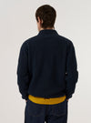 A model wears the Navy Eco Cotton Knit Jacket over a white t-shirt and light-colored trousers against a plain white background. The knit jacket features a button-down front, a classic collar, and two large patch pockets at the waist. The model is shown from the waist up, highlighting the textured knit fabric and relaxed fit of the garment.