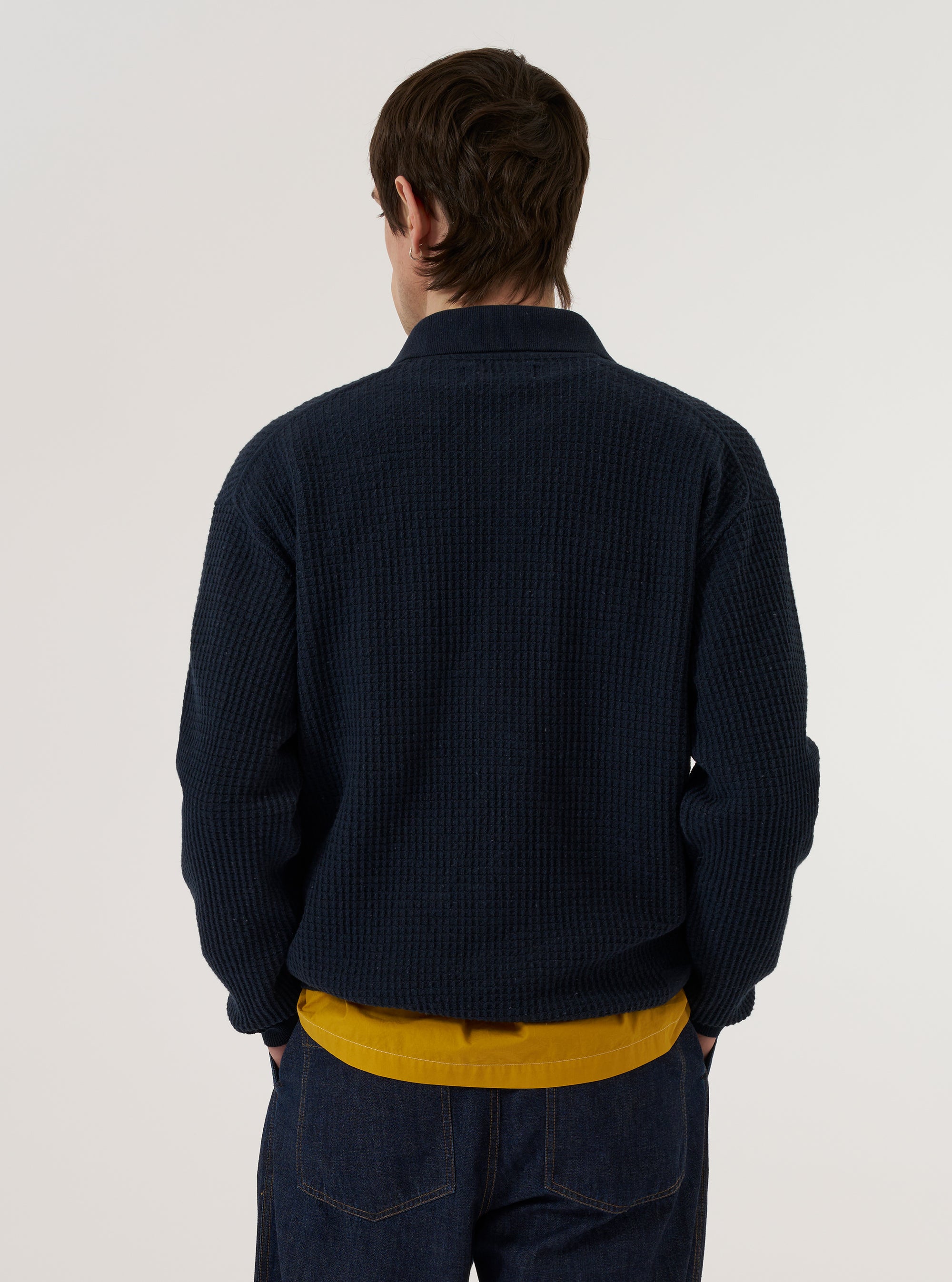 A model wears the Navy Eco Cotton Knit Jacket over a white t-shirt and light-colored trousers against a plain white background. The knit jacket features a button-down front, a classic collar, and two large patch pockets at the waist. The model is shown from the waist up, highlighting the textured knit fabric and relaxed fit of the garment.