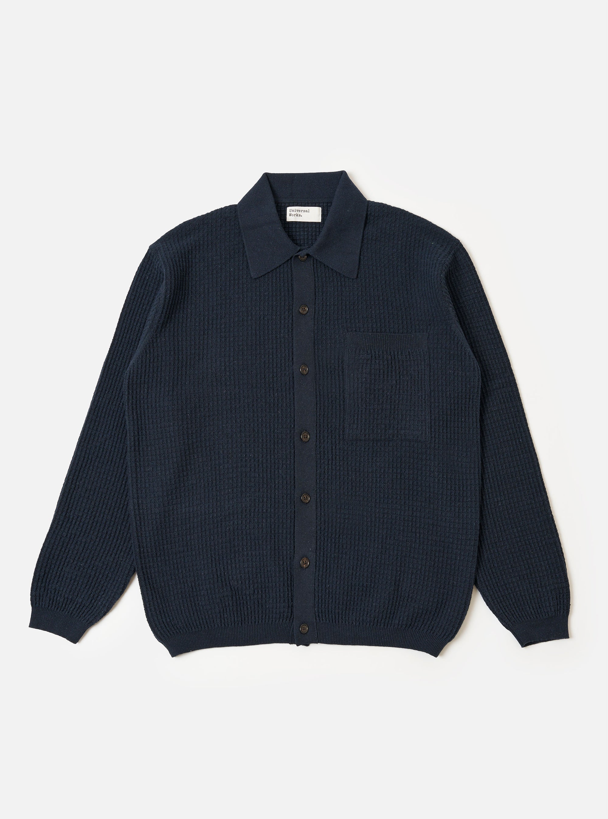 The Navy Eco Cotton Knit Jacket is shown as a flat lay against a white background. This long-sleeve knit jacket features a seven-button front closure, a fully fashioned collar, and a large square patch pocket on the left chest. Ribbed detailing is visible on the collar, cuffs, and hem.
