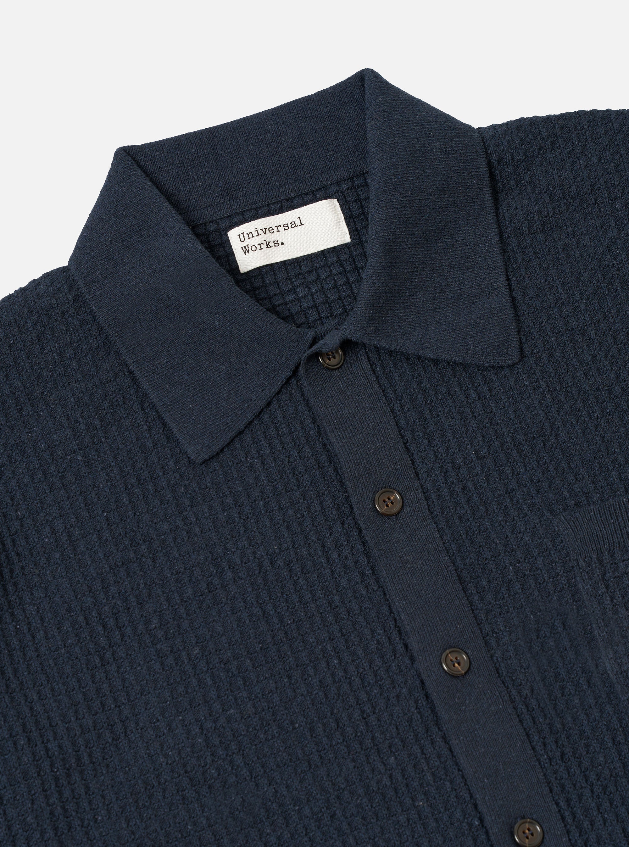 A model wears the Navy Eco Cotton Knit Jacket against a plain, light-grey background. The jacket features a five-button front closure, a structured collar, and two large patch pockets at the waist. The recycled cotton fabric has a visible, fine-gauge knitted texture.