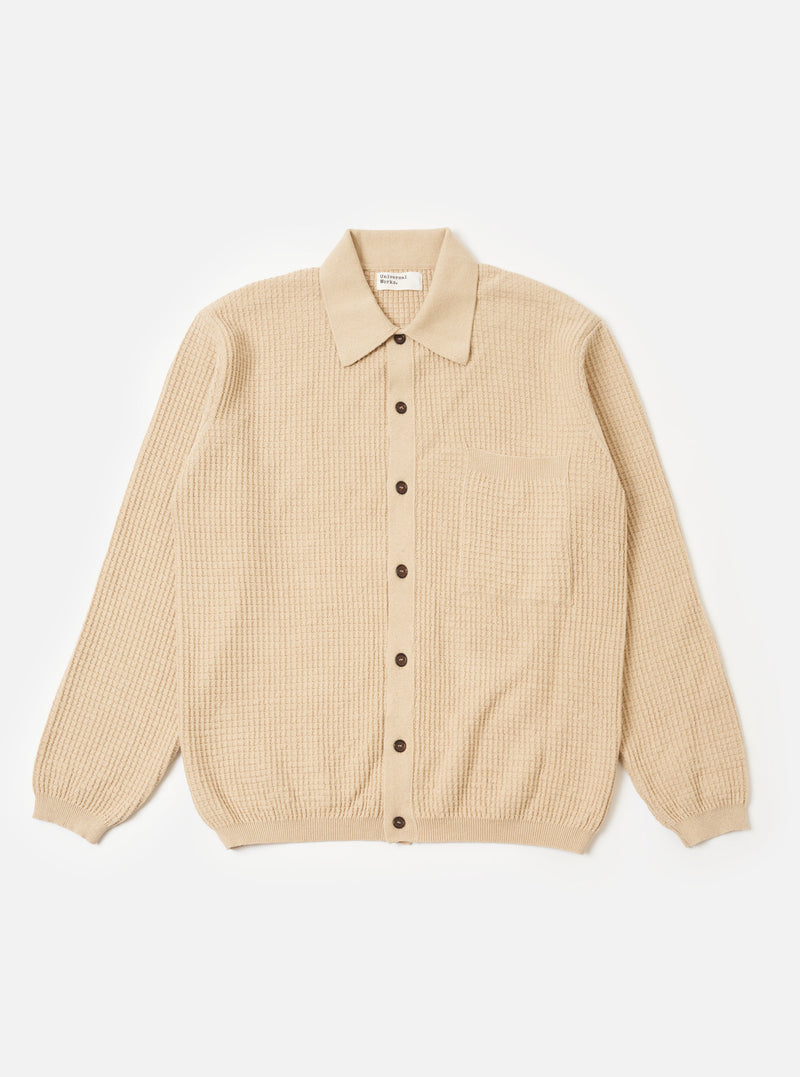 The Sand Eco Cotton Knit Jacket is presented as a flat lay against a white background. The jacket features a full button front, a structured collar, and a large square patch pocket on the left chest. It is designed with a loose fit and finished with rib trims at the cuffs and hem.
