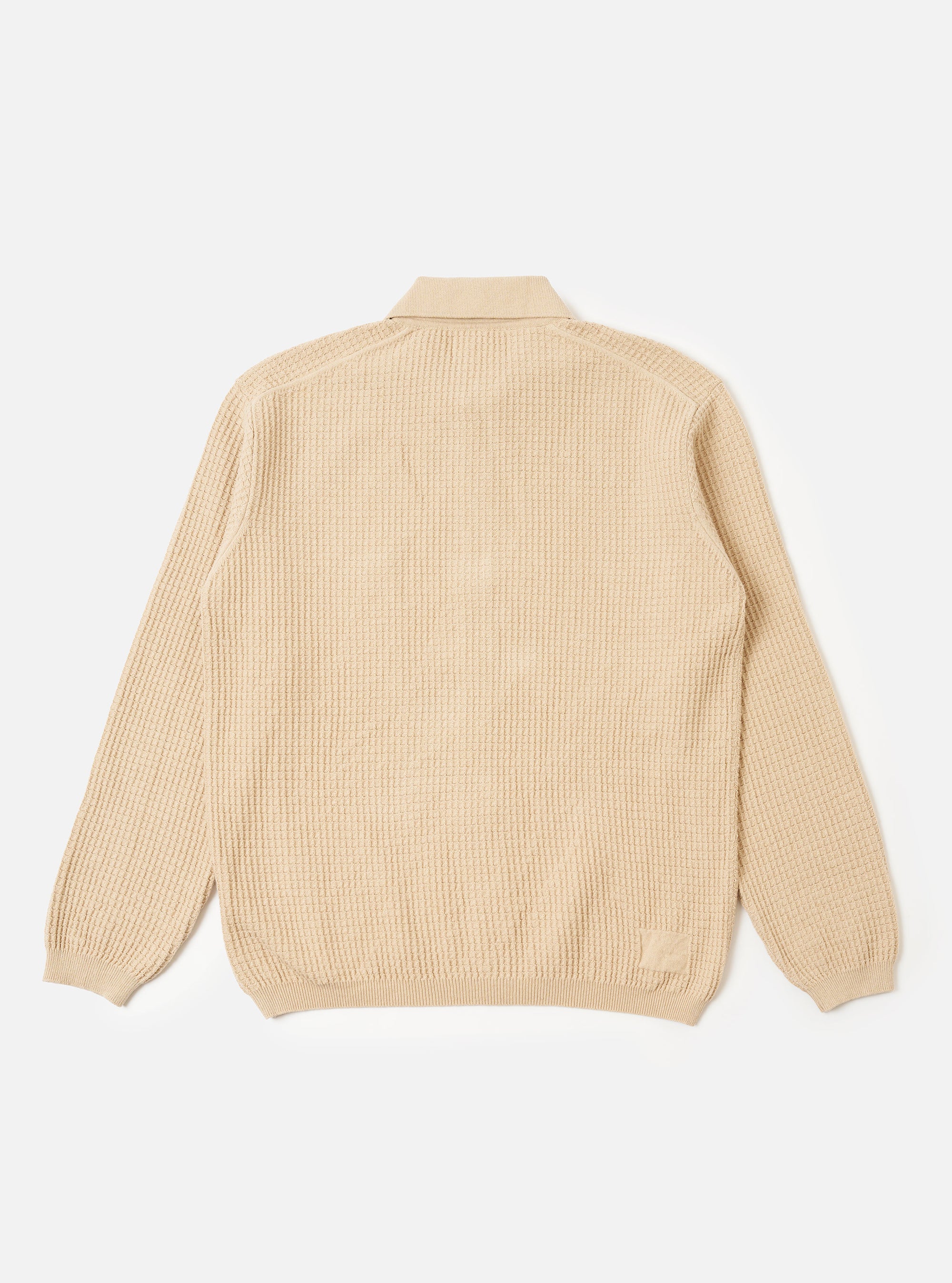 The Sand Eco Cotton Knit Jacket is shown from a rear angle as a flat lay against a white background. The jacket features long sleeves, a straight hem, and ribbed detailing at the cuffs and hem. The knitted fabric has a textured appearance.