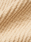 A close-up fabric swatch of the Sand Eco Cotton Knit Jacket shows the textured, ribbed knit of the recycled cotton fabric in detail. The sand-colored material fills the image, highlighting the weave and soft quality of the knitwear.