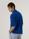 A model is wearing the Blue Woolcot Bio S/S Pullover Knit Shirt II, shown from the back against a plain white background. The image highlights the shirt's relaxed fit, short sleeves, and fine-gauge knit texture in a deep blue hue. The ribbed collar and straight hem are clearly visible as the model stands facing away from the camera.