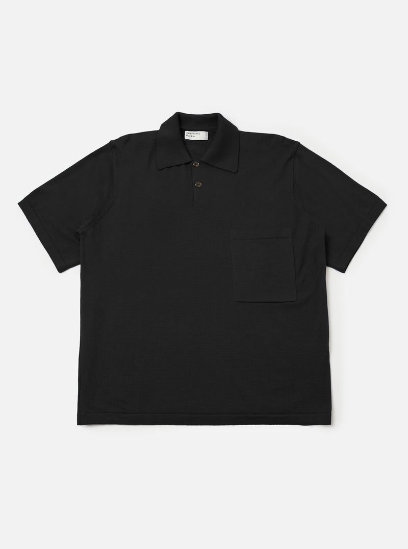 The Black Woolcot Bio S/S Pullover Knit Shirt II is shown as a flat lay against a plain white background. The shirt features a boxy fit, short sleeves, a large collar, and a button placket. A single patch pocket is positioned on the chest. The black fabric has a smooth, fine-knit texture.