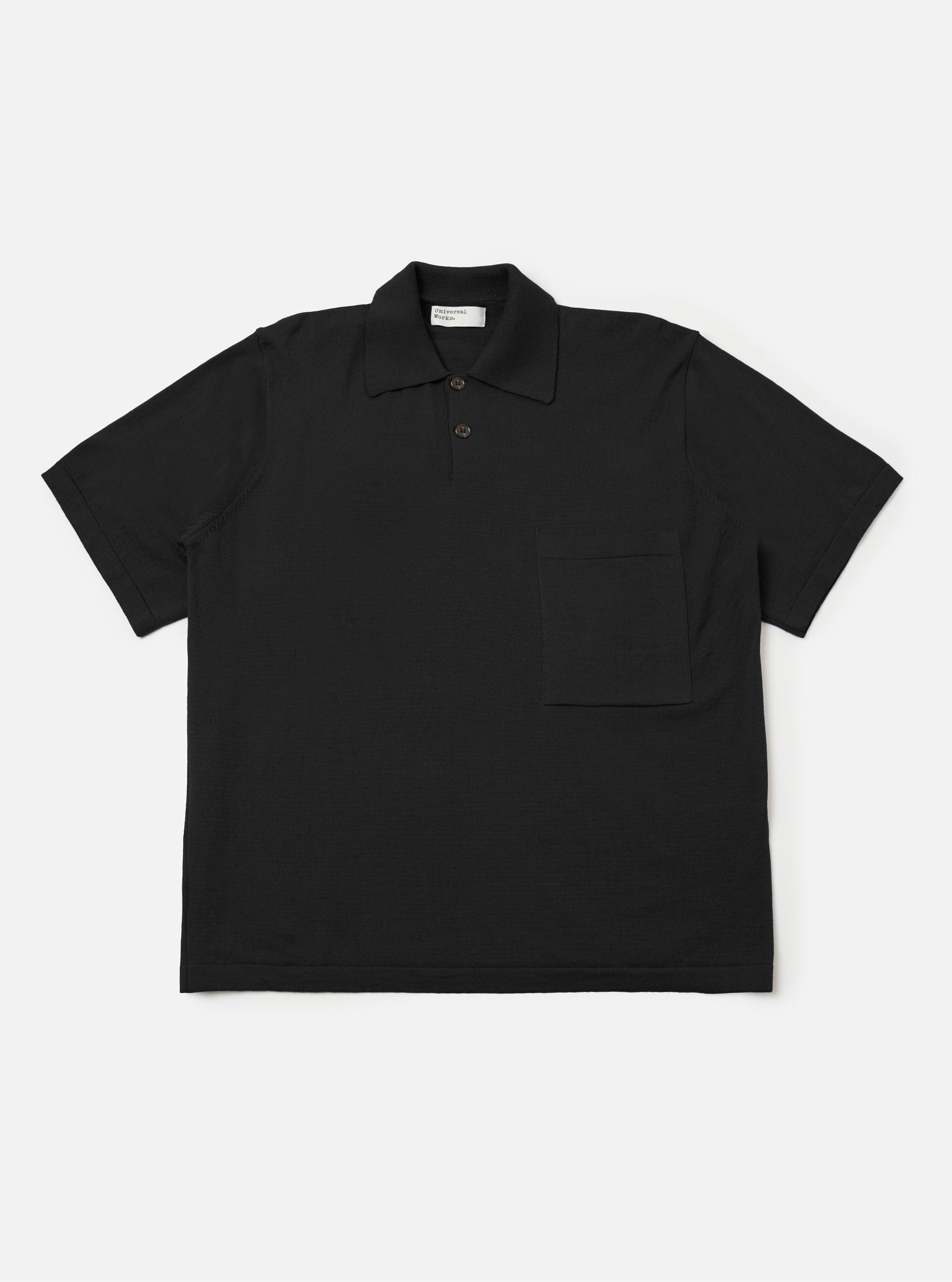 The Black Woolcot Bio S/S Pullover Knit Shirt II is shown as a flat lay against a plain white background. The shirt features a boxy fit, short sleeves, a large collar, and a button placket. A single patch pocket is positioned on the chest. The black fabric has a smooth, fine-knit texture.