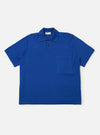 The Blue Woolcot Bio S/S Pullover Knit Shirt II is shown as a flat lay against a white background. The shirt features a boxy fit, short sleeves, a button placket, and a single chest pocket on the left side. The fabric is a smooth, solid blue knit.