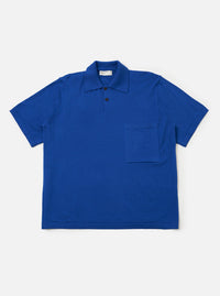 The Blue Woolcot Bio S/S Pullover Knit Shirt II is shown as a flat lay against a white background. The shirt features a boxy fit, short sleeves, a button placket, and a single chest pocket on the left side. The fabric is a smooth, solid blue knit.