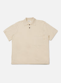 The Ecru Woolcot Bio S/S Pullover Knit Shirt II is shown as a flat lay against a plain white background. This short-sleeved knit shirt features a classic collar, a button placket with two buttons, and a single patch pocket on the left chest. The garment has a boxy fit and is made from a smooth, lightweight ecru-colored knit fabric.