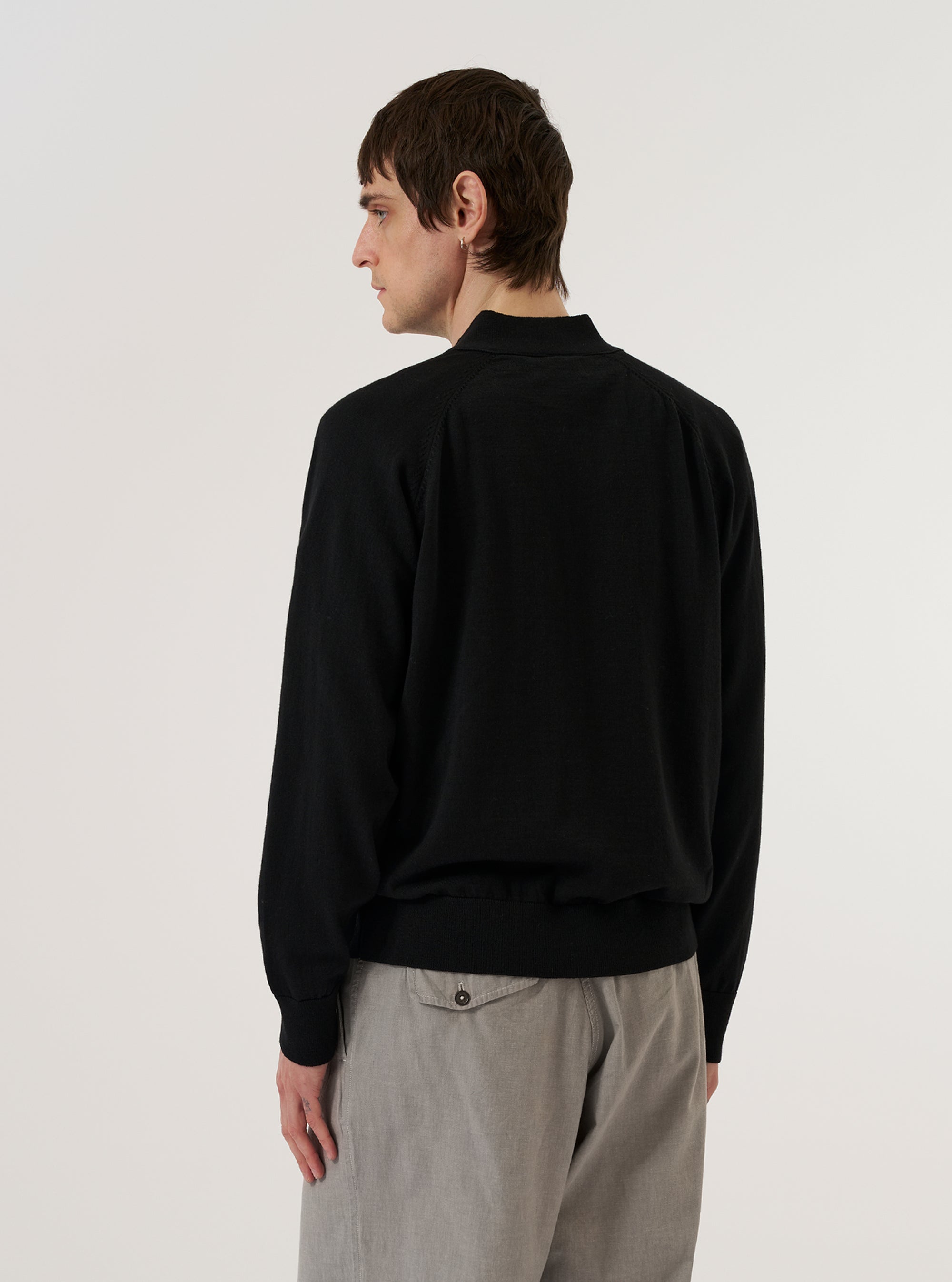 A model wears the Black Woolcot Bio Loose Cardigan II, shown from the back against a plain white background. The cardigan features a relaxed, loose fit with dropped shoulders and ribbed detailing at the cuffs and hem. The garment is constructed from a soft black knit fabric.
