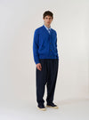 The Blue Woolcot Bio Loose Cardigan II is shown as a flat lay against a plain white background. The cardigan features a V-neckline, a five-button front closure, and two patch pockets at the waist. The garment is constructed from a smooth blue knit with ribbed detailing at the cuffs and hem.