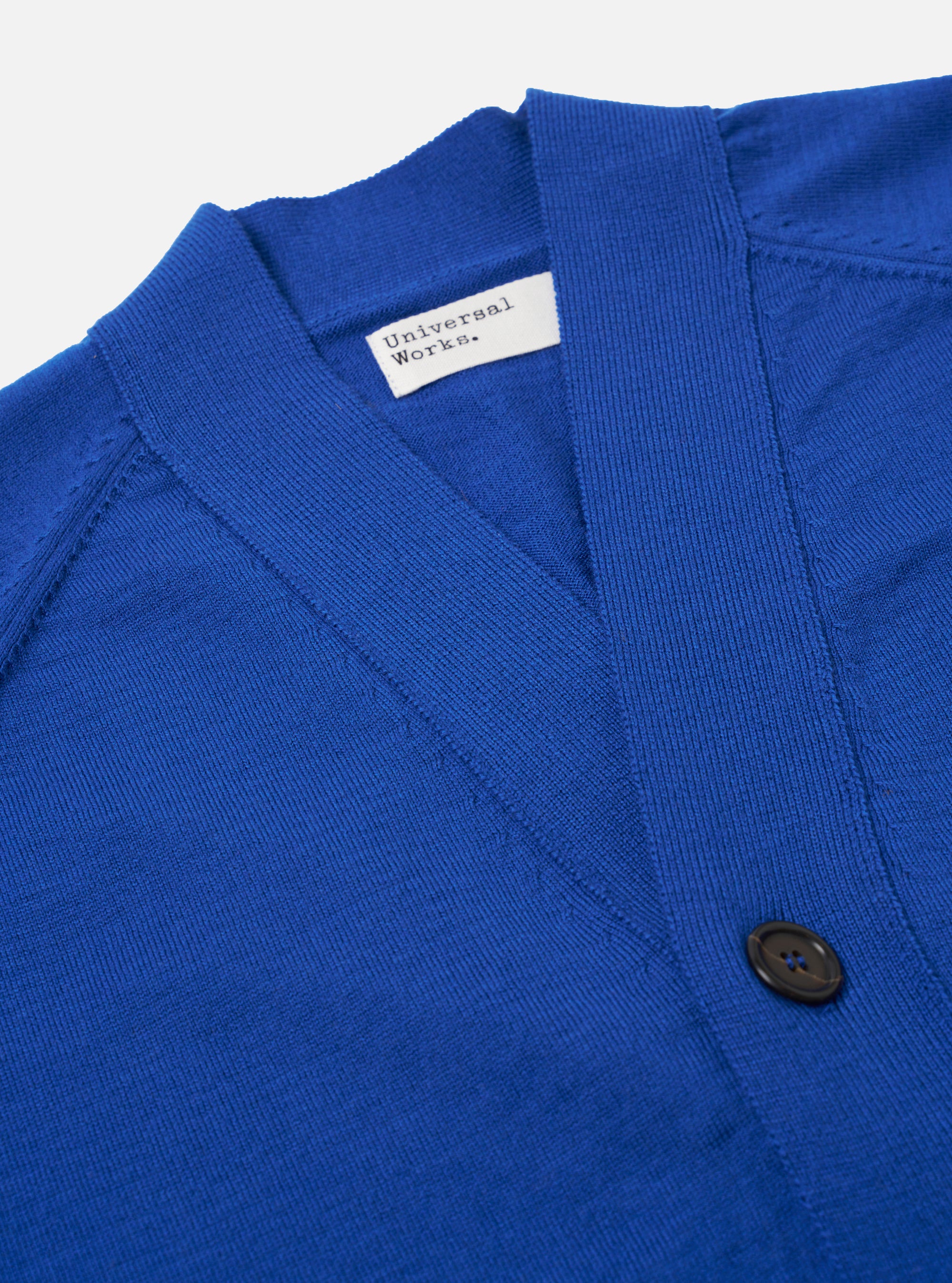 The Blue Woolcot Bio Loose Cardigan II is shown from the back as a flat lay against a plain white background. The image highlights the clean, simple construction of the garment's rear panel and the fine gauge knit texture of the blue merino and organic cotton blend. The ribbed hem and cuffs are clearly visible.