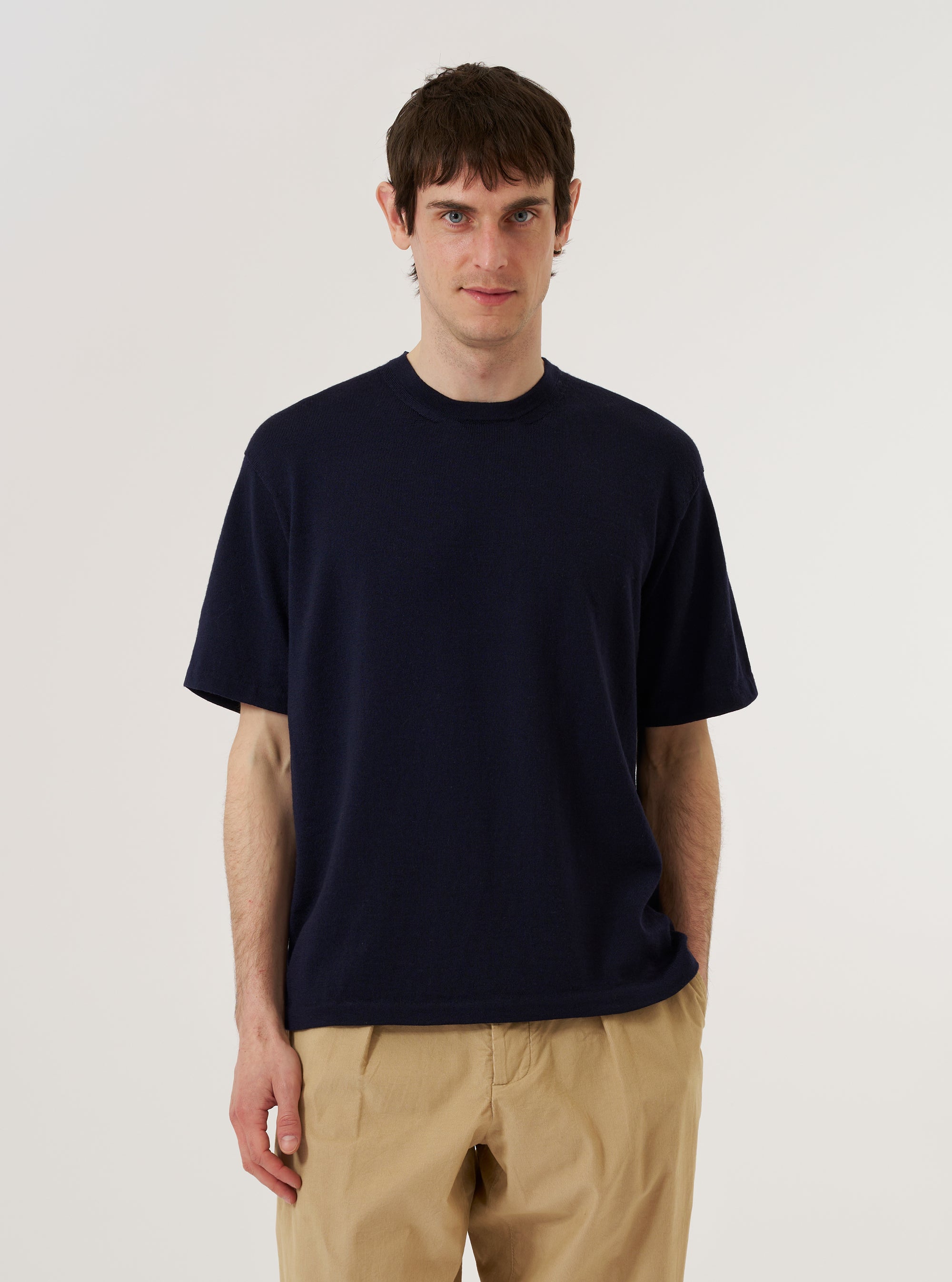 A model wears the Navy Merino Fine Knit Knit Tee against a plain white background. The short-sleeve top features a classic crew neck and a fine-gauge knit texture. The model is shown from the chest up, highlighting the garment's smooth finish and clean-lined fit. No other accessories or layers are visible in the image.