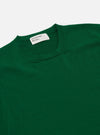 A model wears the Green Merino Fine Knit Knit Tee shown from a rear three-quarter view against a plain, light-colored background. The garment is a short-sleeved t-shirt made from a fine merino wool knit, featuring a ribbed crew neck, ribbed cuffs, and a ribbed hem. The fit is relaxed, and the model is shown from the waist up.
