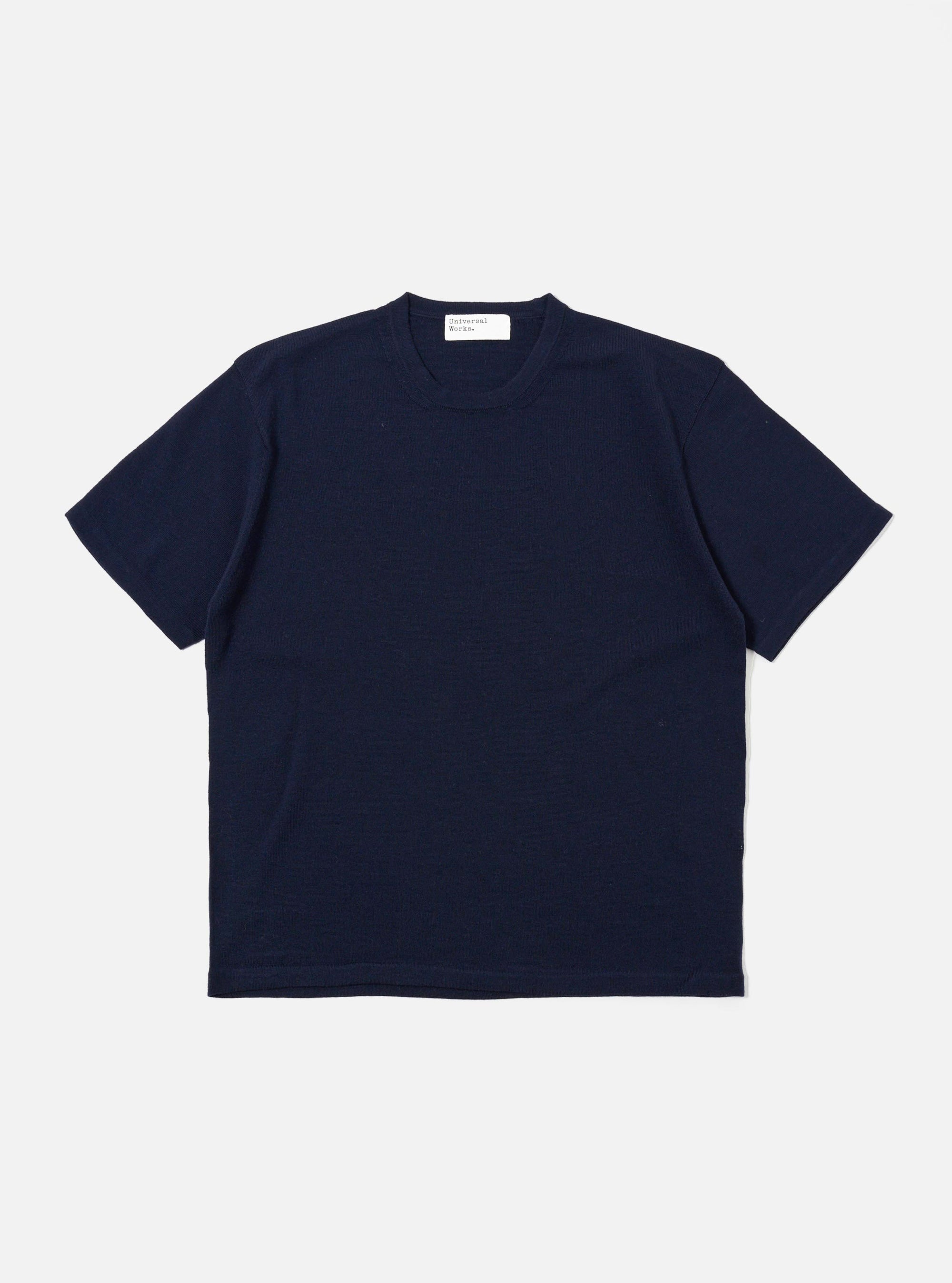 The Navy Merino Fine Knit Knit Tee is displayed as a flat lay against a white background. The short-sleeved garment features a crew neck, ribbed cuffs, and a ribbed hem. The fine merino wool knit provides a smooth, uniform texture throughout.