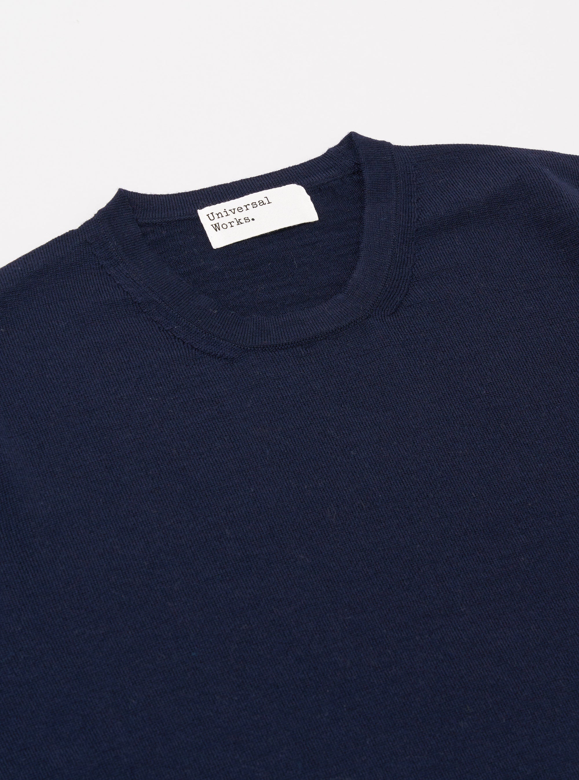 A model wears the Navy Merino Fine Knit Knit Tee against a plain, light-colored background. The image highlights the garment's fine-gauge merino wool texture, featuring a ribbed crew neckline and short sleeves.