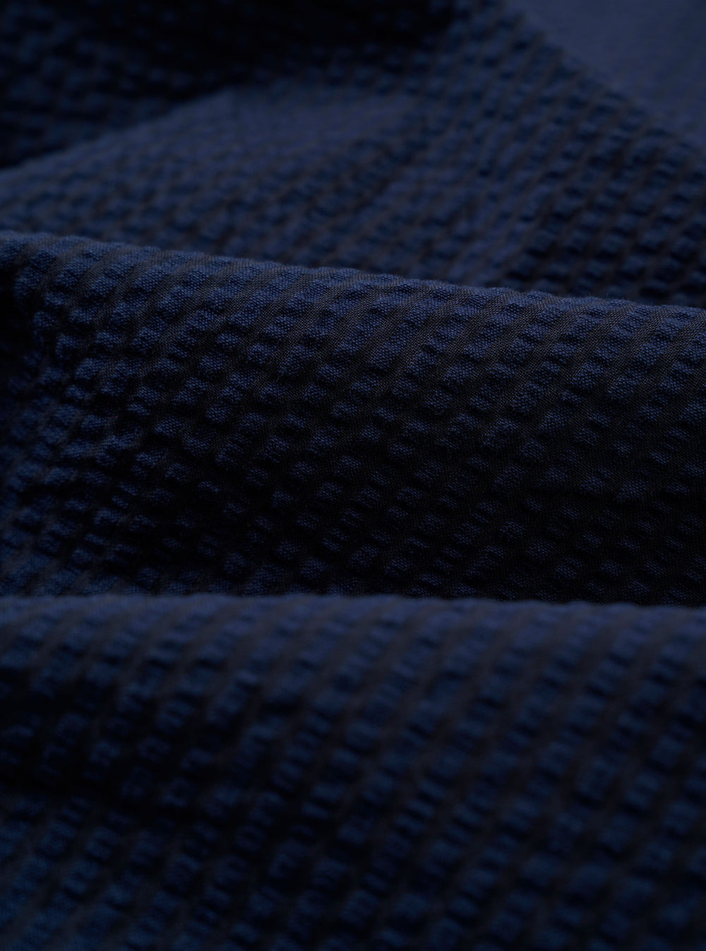 A close-up swatch image of the Navy Derby Stripe Two Button Jacket fabric shows a dark navy blue base with a thin, vertical white stripe pattern. The cotton material is displayed in detail, highlighting the texture and color of the suiting fabric.