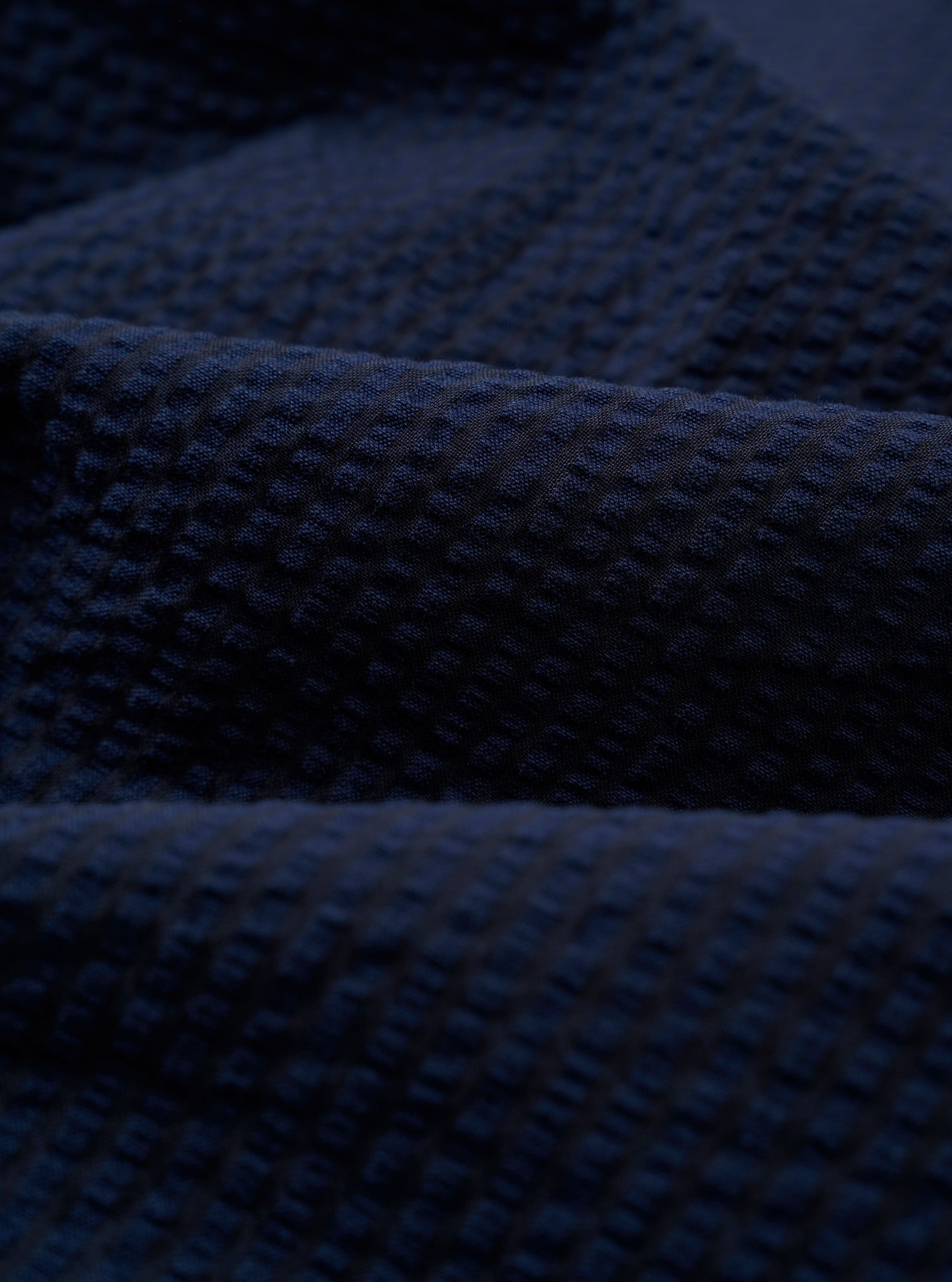A close-up swatch image of the Navy Derby Stripe Two Button Jacket fabric shows a dark navy blue base with a thin, vertical white stripe pattern. The cotton material is displayed in detail, highlighting the texture and color of the suiting fabric.