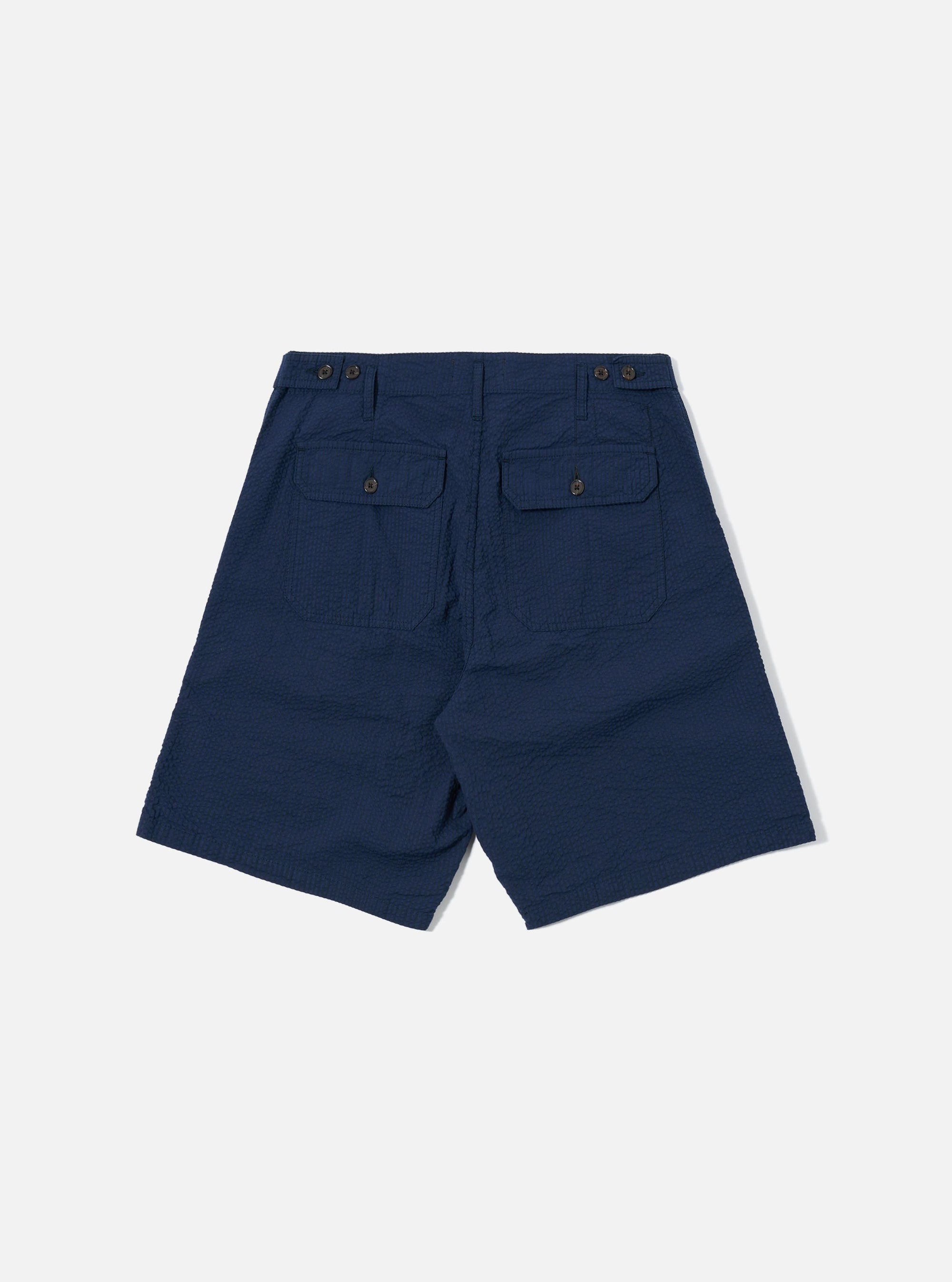 The Navy Derby Stripe Clean Short is shown from the back as a flat lay against a plain white background. The image highlights the clean construction of the rear, featuring a single patch pocket on the right side and an elasticated waistband with visible stitching. The cotton fabric has a pattern of thin, vertical navy blue and white stripes.