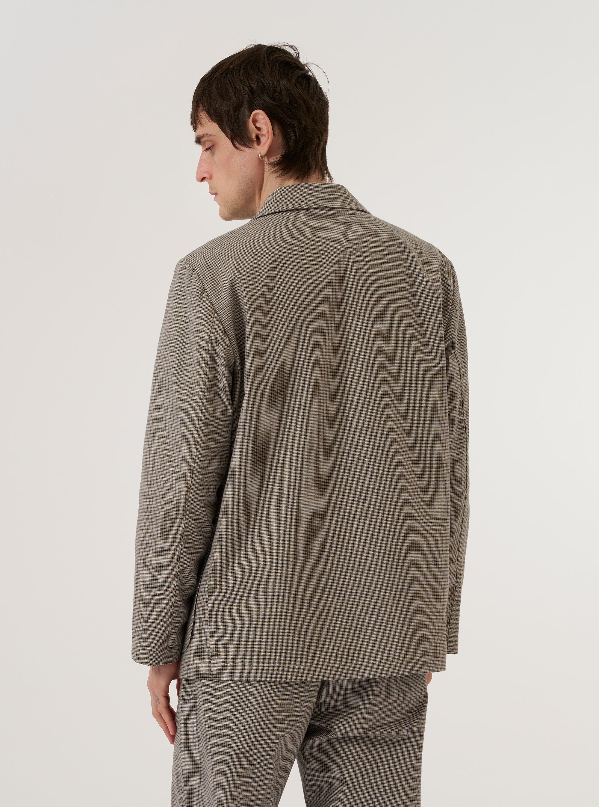 A model wears the Multi Lucas Cotton Mix Two Button Jacket, shown from a rear three-quarter angle against a plain white background. The jacket features a prominent multi-colored check pattern, a central rear vent, and a structured fit. The model is wearing the jacket over a dark top and matching trousers.