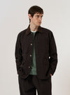 A model is wearing the Licorice Summer Canvas Labour Jacket over a light-colored top, standing against a plain white background. The jacket features a classic collar, a button-down front, two chest patch pockets, and two lower patch pockets with flap closures. The fabric is a solid brown licorice color with a sturdy canvas texture.