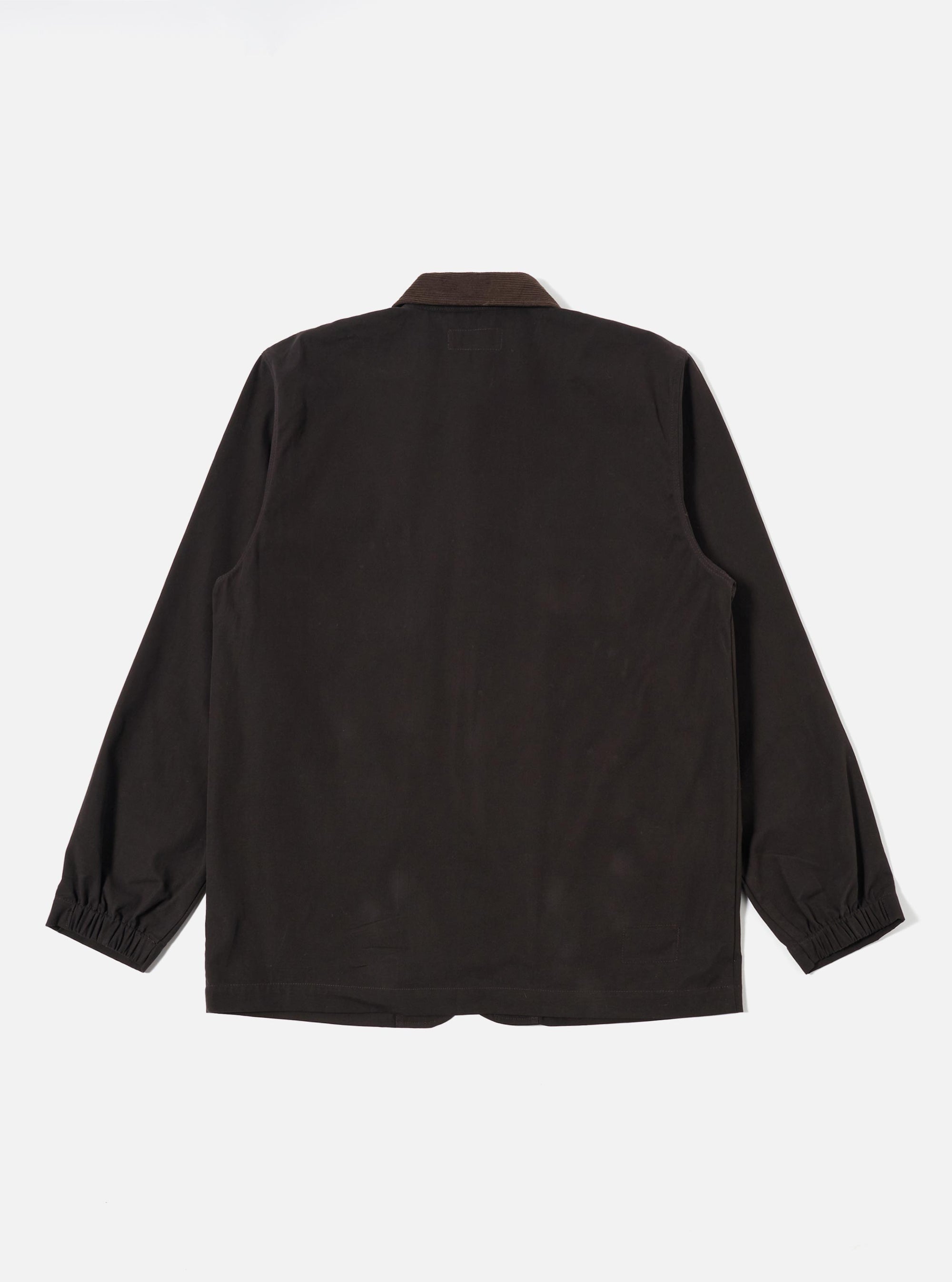 A model wears the Licorice Summer Canvas Labour Jacket against a plain, light-colored background. The jacket features four front patch pockets, with two chest pockets and two lower pockets that include buttoning flaps. The garment is shown in a loose, wide fit with a five-button front closure and a traditional collar. The fabric is a cotton canvas with a textured, matte finish.