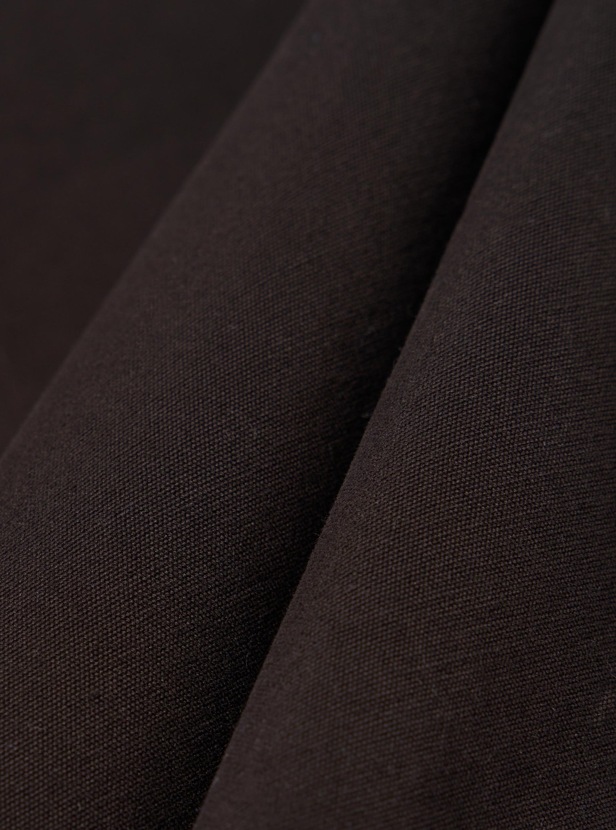 A close-up fabric swatch of the Licorice Summer Canvas Labour Jacket highlights a deep brown color and a durable, woven canvas texture. The image shows the material as a solid, flat surface with a subtle, suede-like finish.
