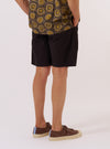 A model is wearing the Licorice Summer Canvas Clean Short, shown from the waist down against a plain, neutral background. The shorts feature a relaxed fit and are made from a dark brown licorice-colored cotton canvas. The garment has a clean-cut appearance with visible side pockets and a structured waistband.