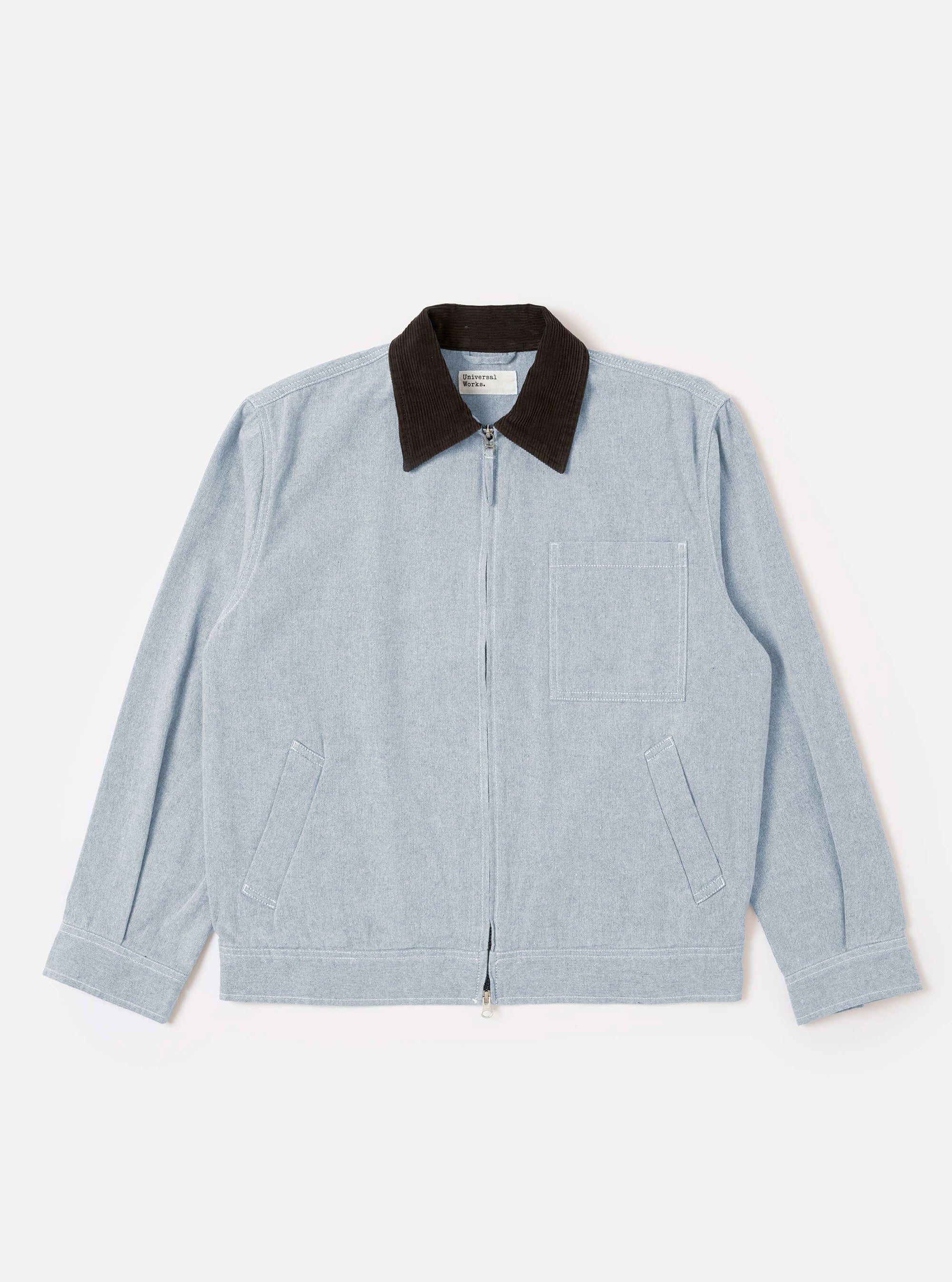 The Light Indigo Jean Cloth Reworked Rose Bowl Jacket is shown as a flat lay against a white background. The jacket features a double-ended zip front, a structured collar, one large chest patch pocket, and two side welt pockets. The light indigo fabric is made from a reworked organic cotton blend with a visible denim-like texture.