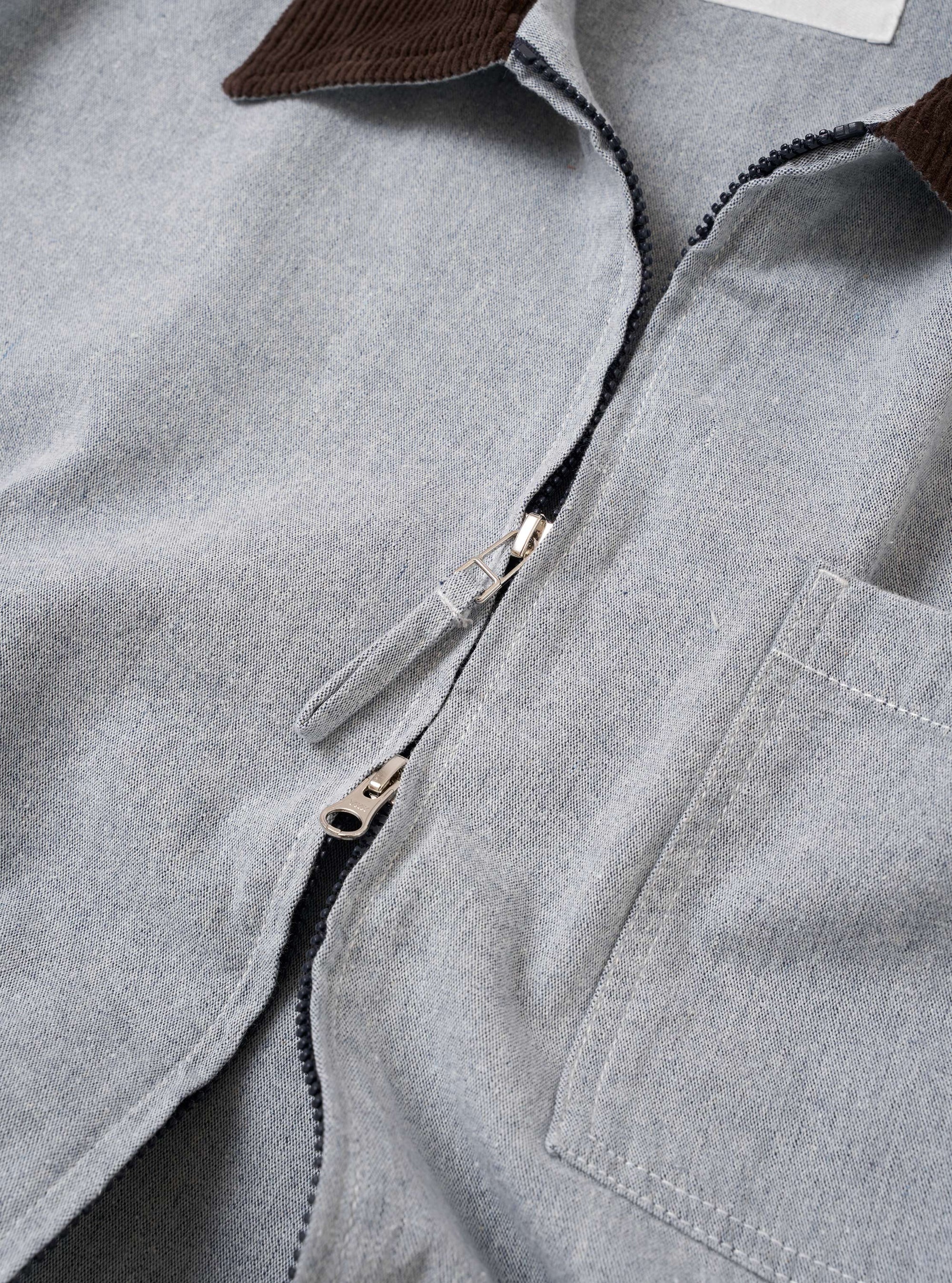 The Light Indigo Jean Cloth Reworked Rose Bowl Jacket is shown from the back as a flat lay against a plain white background. The jacket features a clean, simple construction with a straight hem, a pointed collar, and a locker loop at the nape. The light indigo organic cotton fabric displays a smooth texture and tonal stitching.