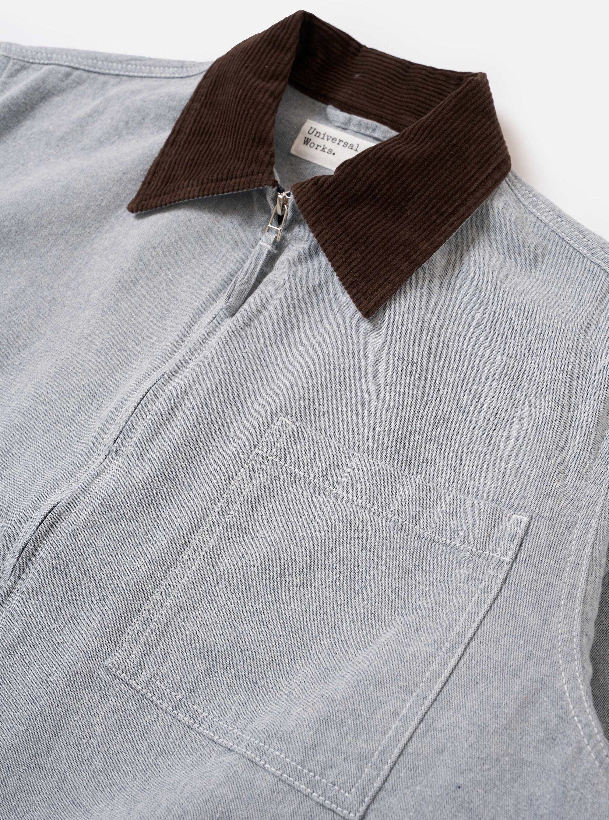 The Light Indigo Jean Cloth Reworked Rose Bowl Jacket is shown from the back as a flat lay against a plain white background. The image highlights the boxy fit, slightly oversized collar, and functional details including buttoned adjustable cuffs and an adjustable back hem with pleats. The light indigo organic cotton fabric features a clean, uniform finish.