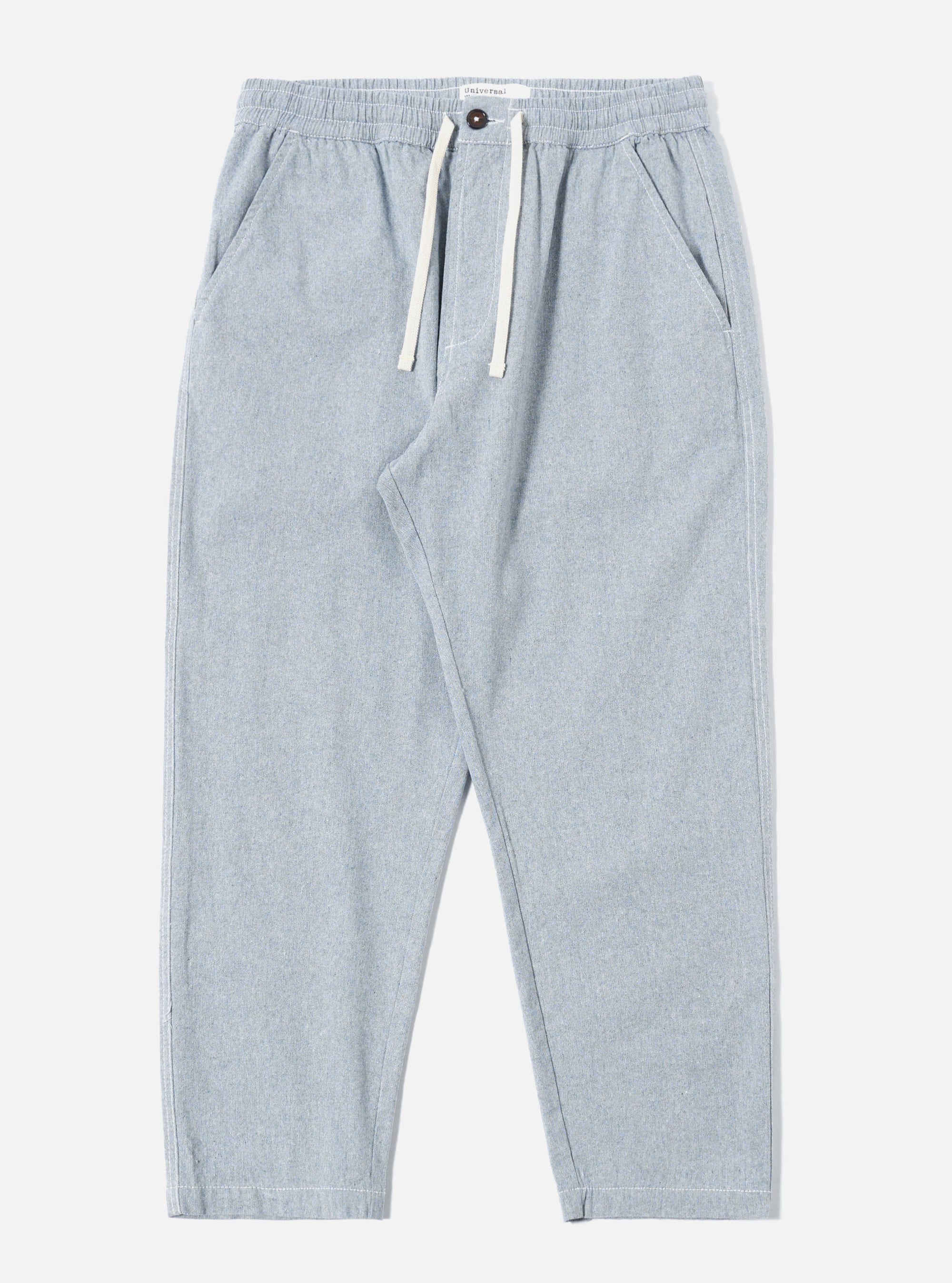 The Light Indigo Jean Cloth Reworked Hi Water Trouser is shown as a flat lay against a white background. The trousers feature a drawstring waist, two slanted front pockets, and a slightly cropped, loose fit. The fabric is a light indigo organic cotton with a visible textured weave.
