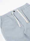 The Light Indigo Jean Cloth Reworked Hi Water Trouser is shown from a rear angle as a flat lay against a plain white background. The image highlights the two back patch pockets and the elasticated drawstring waistband. The light indigo organic cotton fabric features a visible textured weave and a slightly cropped leg length.