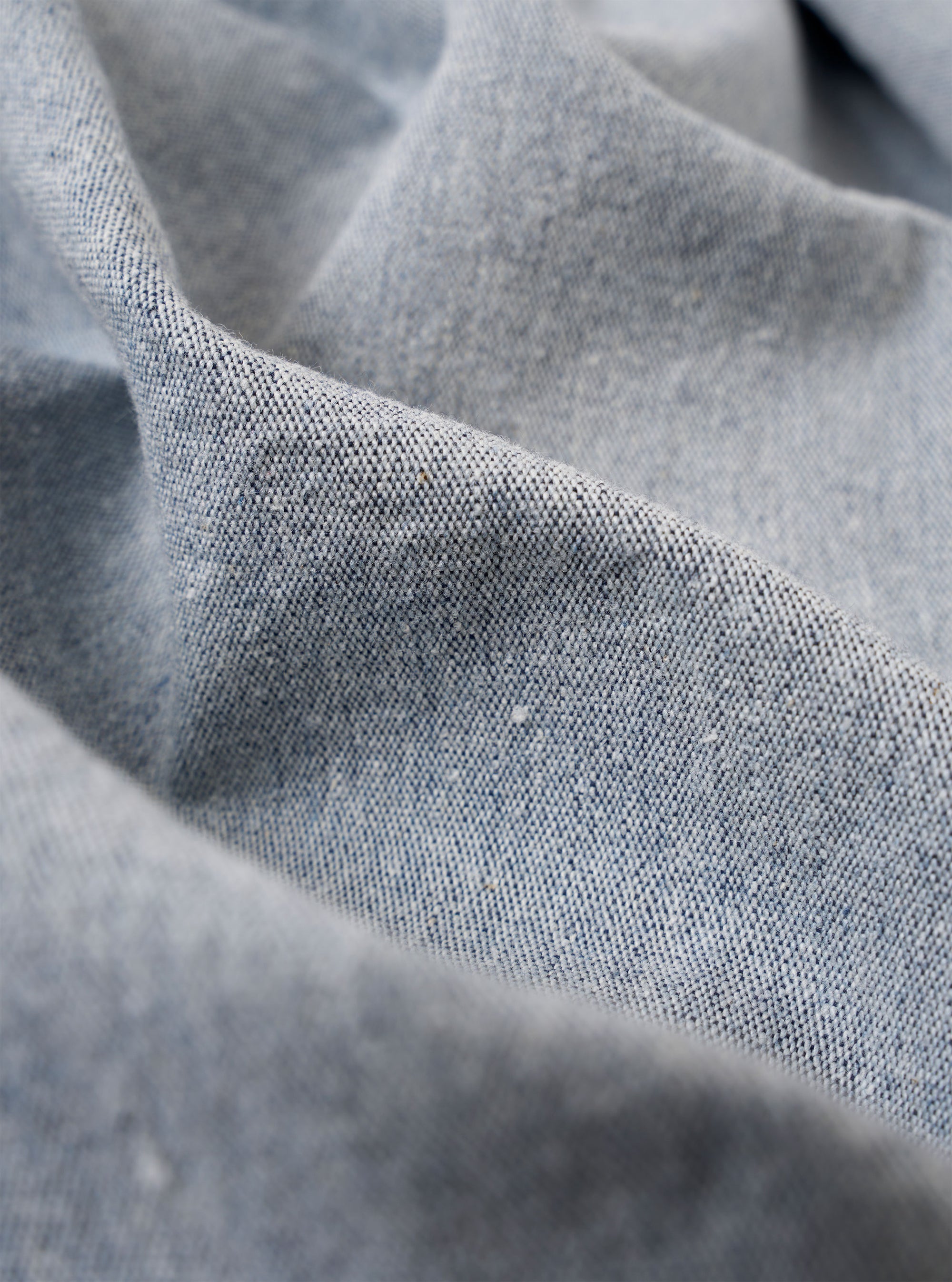 A close-up fabric swatch of the Light Indigo Jean Cloth Reworked Duke Pant highlights the light blue indigo-dyed organic cotton material. The image focuses on the textured weave of the fabric, filling the entire frame.