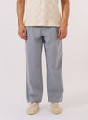 A model wears the Light Indigo Jean Cloth Reworked Duke Pant, shown from the waist down against a plain white background. The trousers feature a wide, straight leg with a single pleat at the front and a fixed waistband. The light indigo organic cotton fabric has a soft, washed appearance. The model is wearing the pants with white socks and brown shoes.