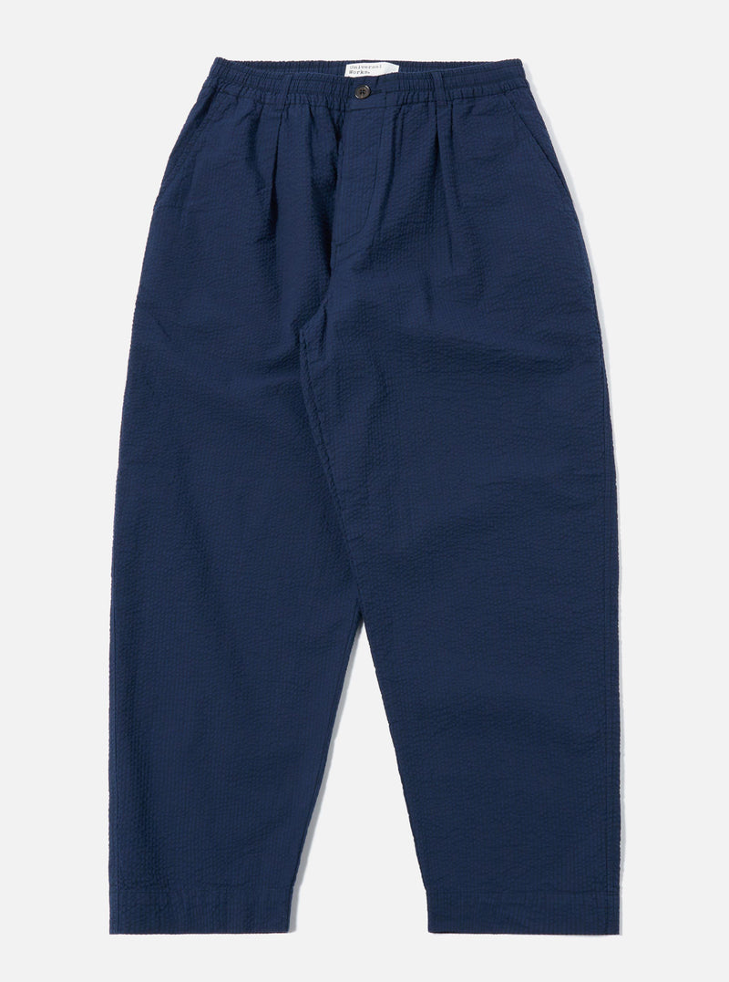 The Navy Derby Stripe Oxford Pant is shown as a flat lay against a plain white background. The trousers feature a vertical navy and white stripe pattern, a wide-leg fit, and double pleats at the waist. The design includes an elasticated waistband with an external drawstring and two side pockets.