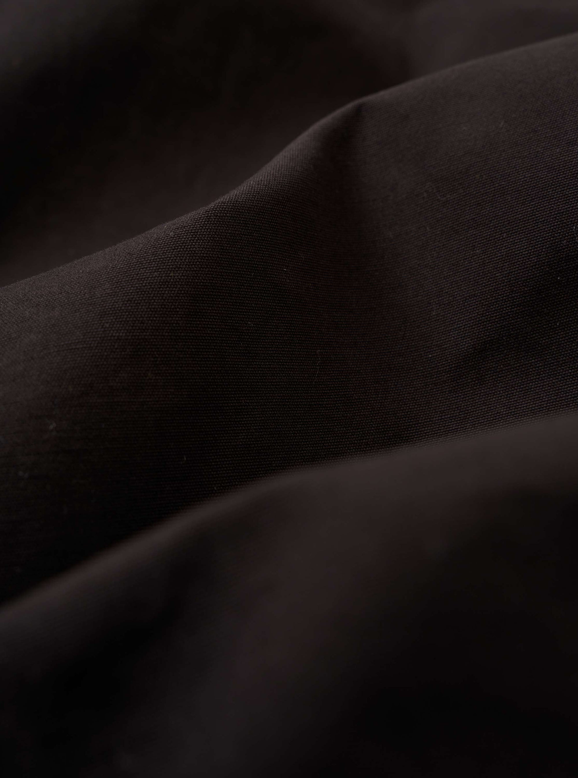 A close-up fabric swatch of the Licorice Summer Canvas Two Button Jacket highlights the dark brown, licorice-colored cotton canvas. The image provides a detailed view of the material's weave and slightly textured, suede-like surface.
