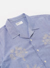 The Blue Oxford Shirting Road Trip Shirt is shown as a flat lay against a white background. The shirt is a light blue, short-sleeved button-up with a regular fit and a straight hem. It features a single-piece loop-close collar, a single chest patch pocket, and tonal buttons.