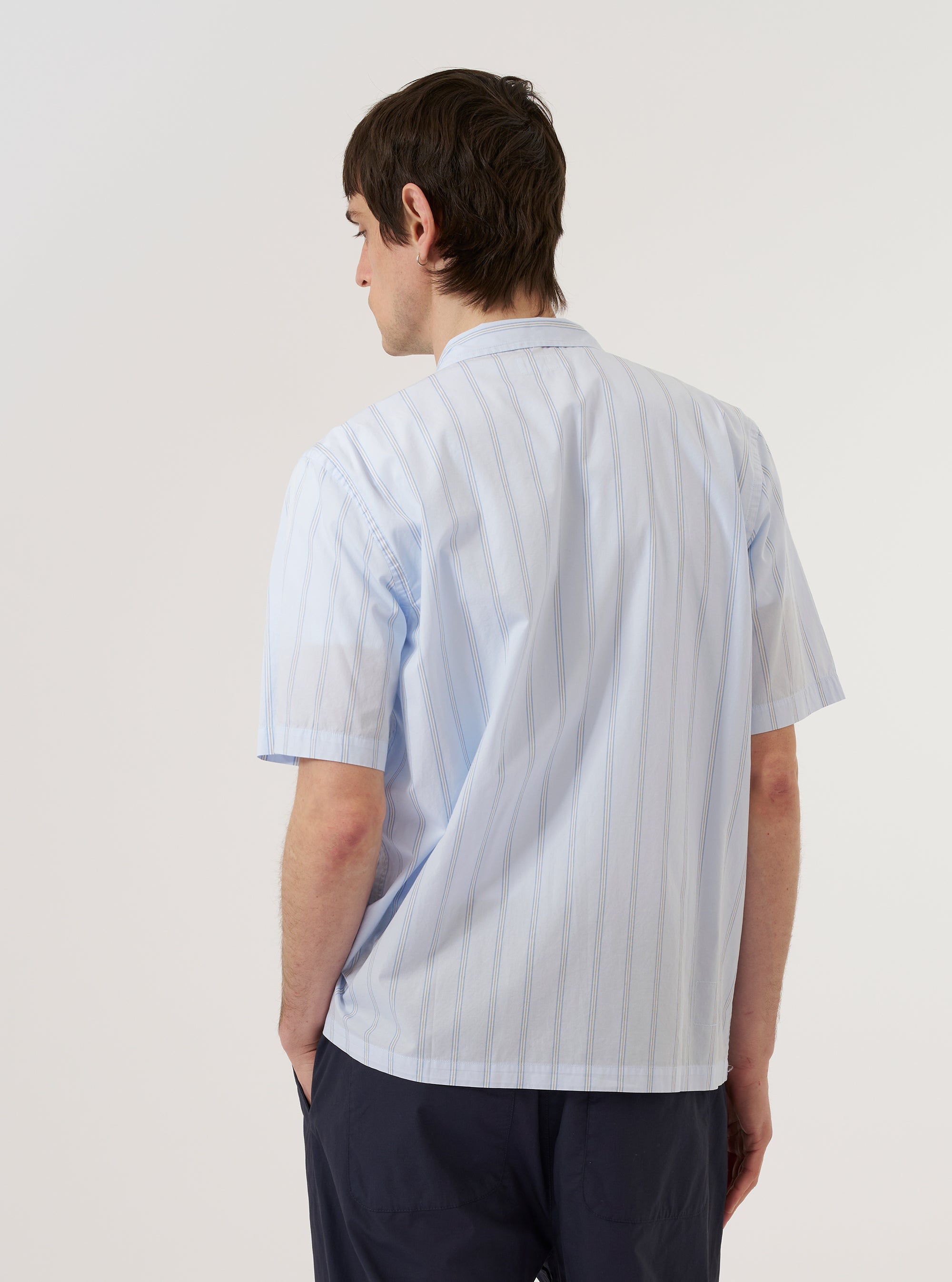 A model wears the Soft Blue Mc Stripe Road Trip Shirt against a plain white background. The shirt features a vertical stripe pattern in soft blue and white, a camp collar, and a single chest pocket. The image shows the model from the waist up, highlighting the fit and collar detail.