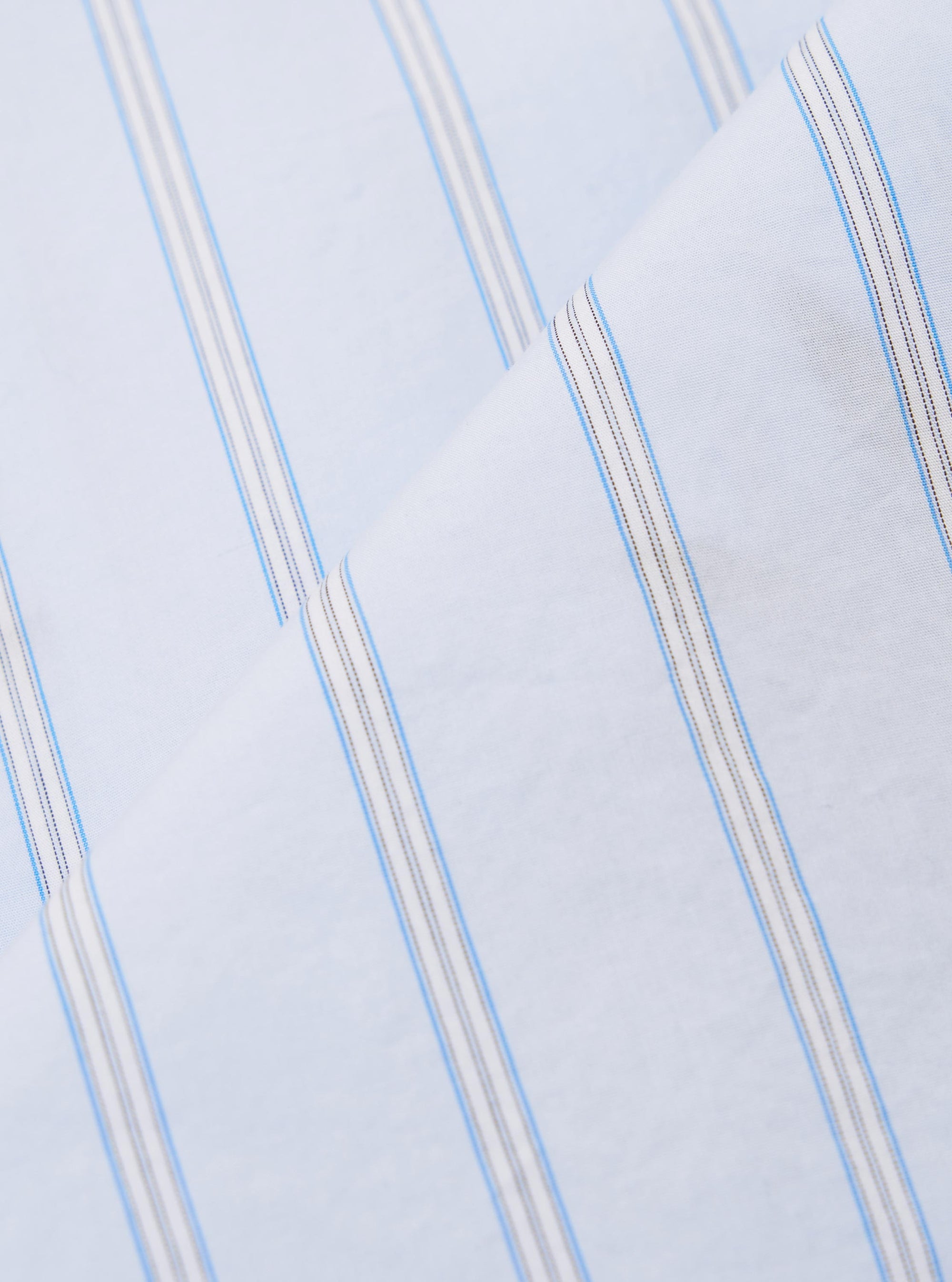 A close-up swatch image of the Soft Blue Mc Stripe Road Trip Shirt fabric displays a detailed view of the light blue and white vertical stripes. The textile has a visible woven texture with a fine grain, and the edges of the swatch are finished with a zigzag pinked cut.