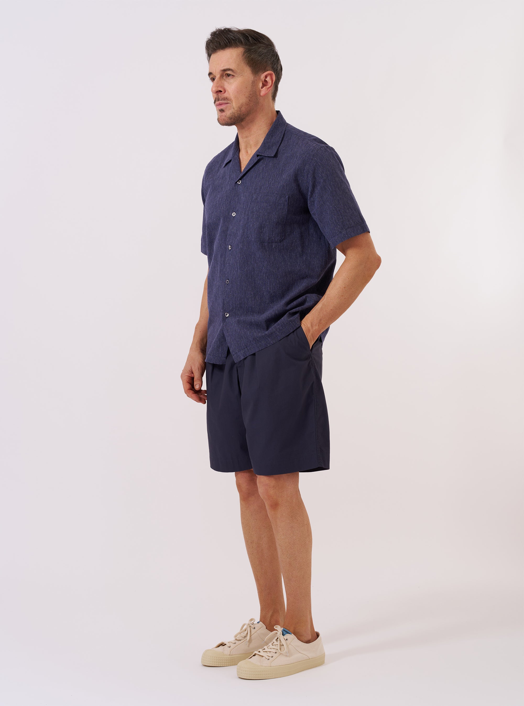 A model wears the Navy Sido Linen Mix Road Shirt over a light-colored top, standing against a plain white background. The shirt features a camp collar, a button-front closure, and a single chest pocket. The fabric has a visible textured linen-mix weave in a deep navy blue.