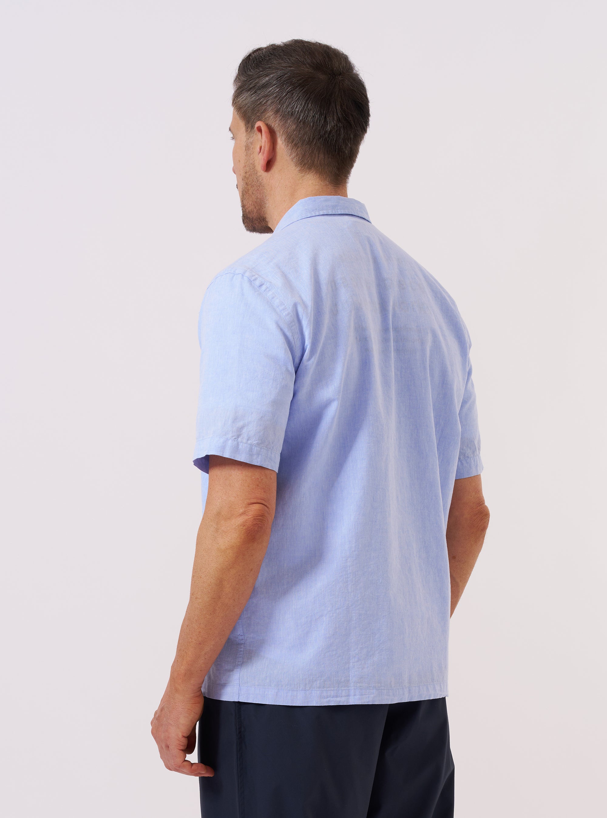 A model wears the Sky Blue Sido Linen Mix Road Shirt, shown from the back against a plain white background. The shirt features a relaxed fit, a straight hem, and a simple back yoke. The sky blue fabric has a visible linen-blend texture with a subtle, multi-tonal weave. No mannequin is present in the image.