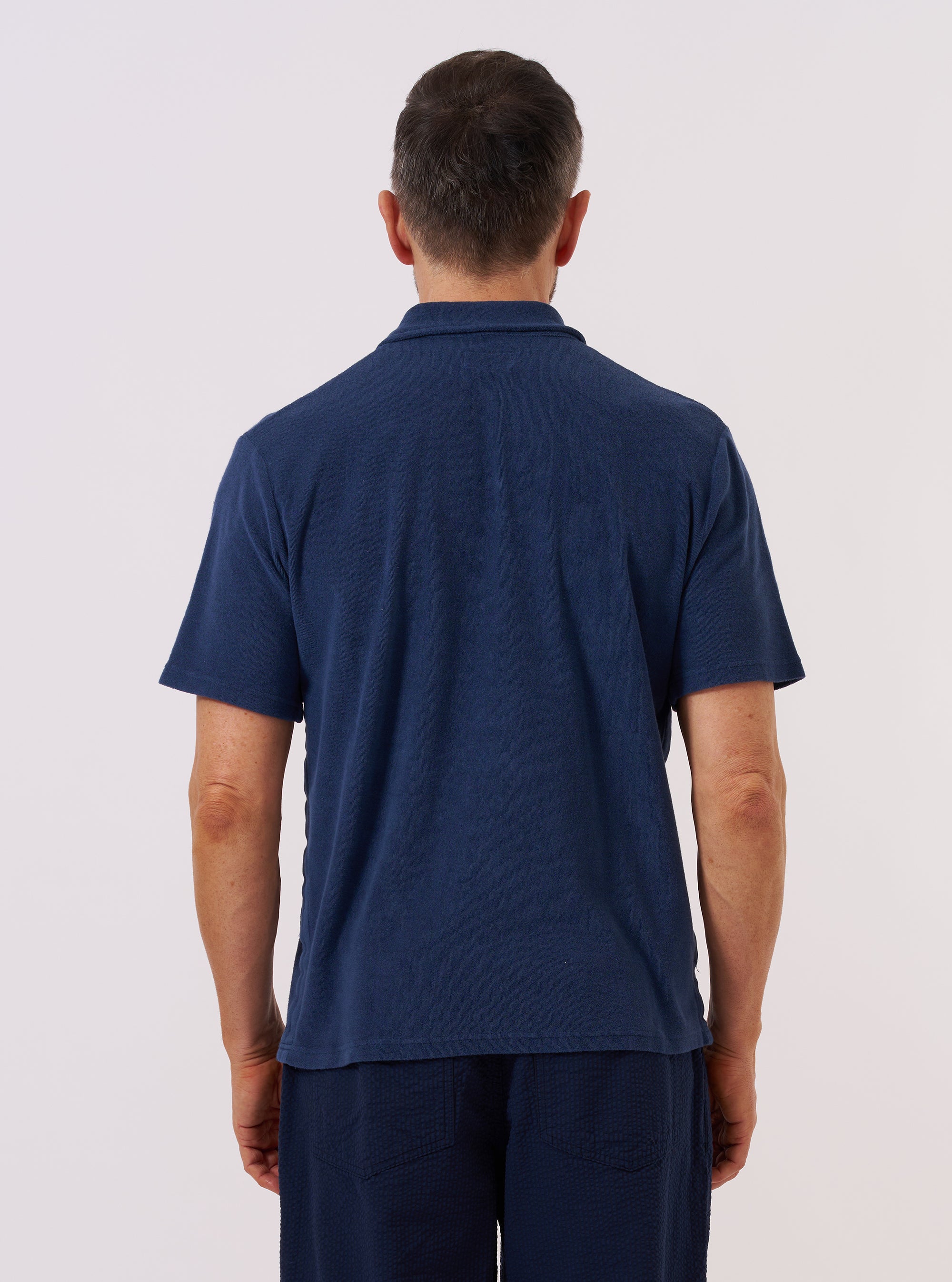 A model is wearing the Indigo Lincot Denim Road Shirt over a white t-shirt, shown from the side against a plain white background. The shirt features a camp collar, a single chest patch pocket, and a button-front closure. The denim fabric is a deep indigo blue with a slightly textured appearance.