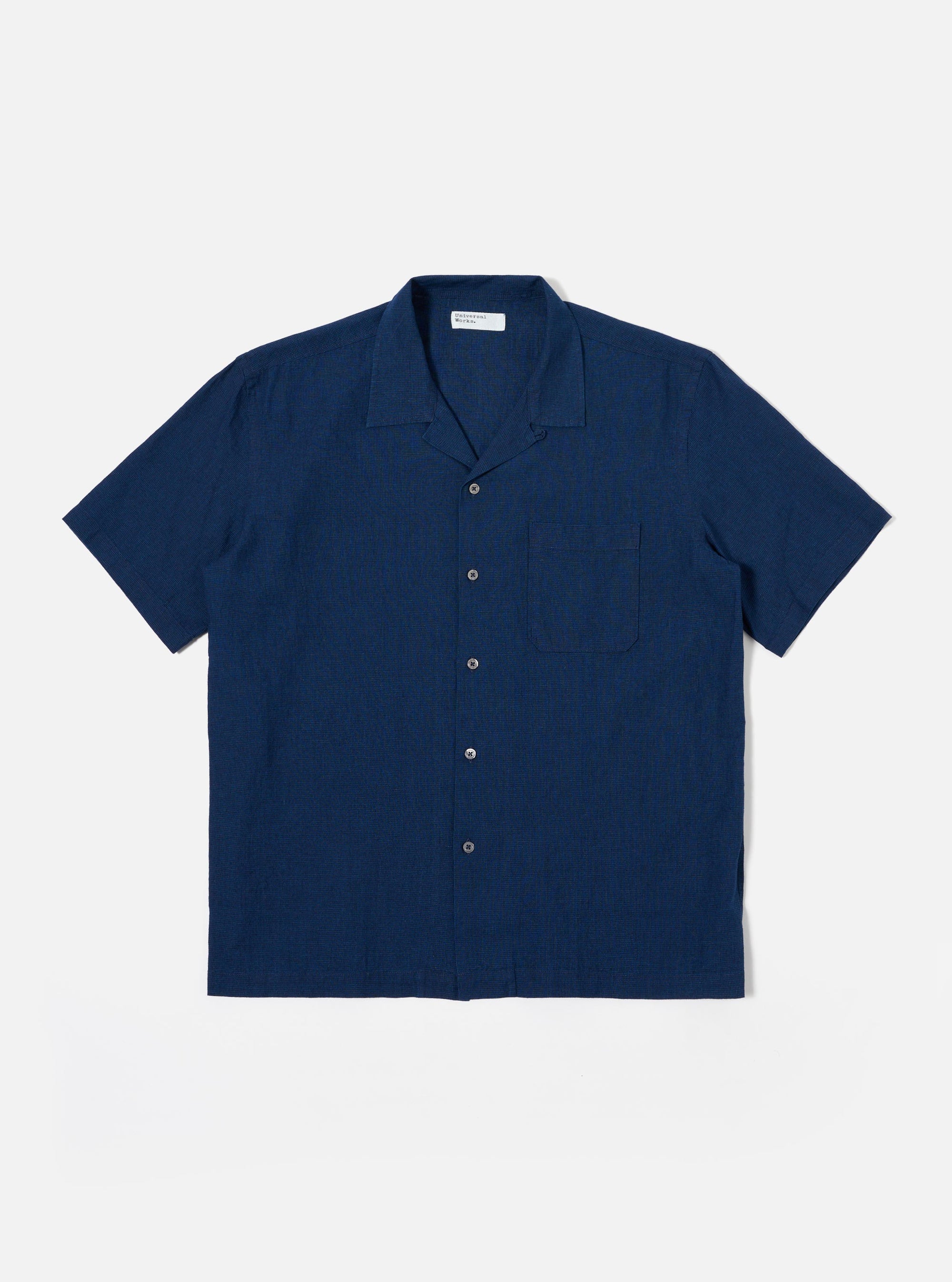 The Indigo Lincot Denim Road Shirt is presented as a flat lay against a plain white background. The short-sleeved shirt features a camp collar, a six-button front closure with contrasting white buttons, and a single patch pocket on the left chest. The indigo-dyed fabric shows a fine denim texture from the cotton and linen blend.