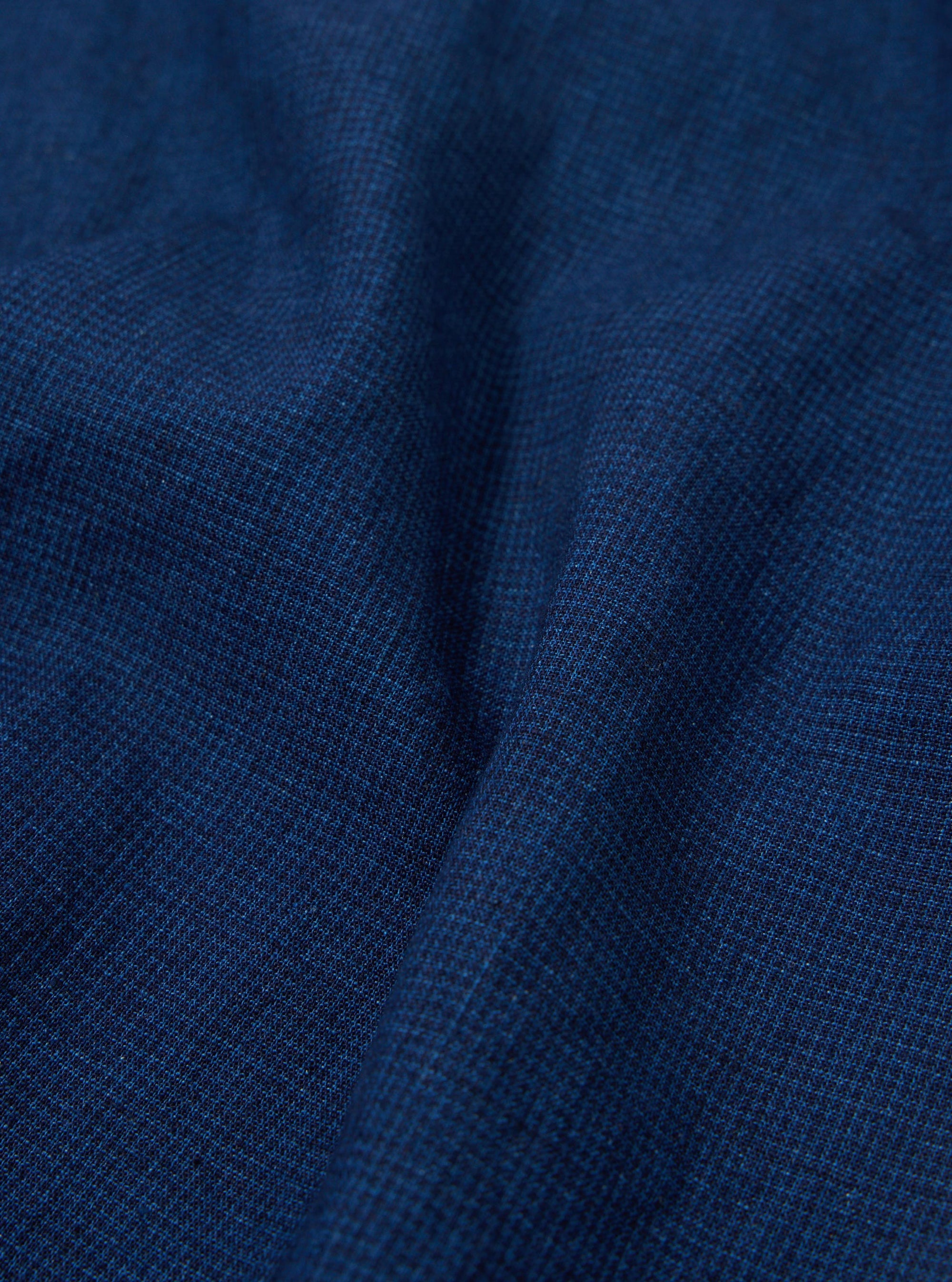 A close-up swatch image of the Indigo Lincot Denim Road Shirt fabric displays a deep indigo blue color with a visible diagonal twill weave and subtle white-flecked texture. The fabric appears midweight and structured.