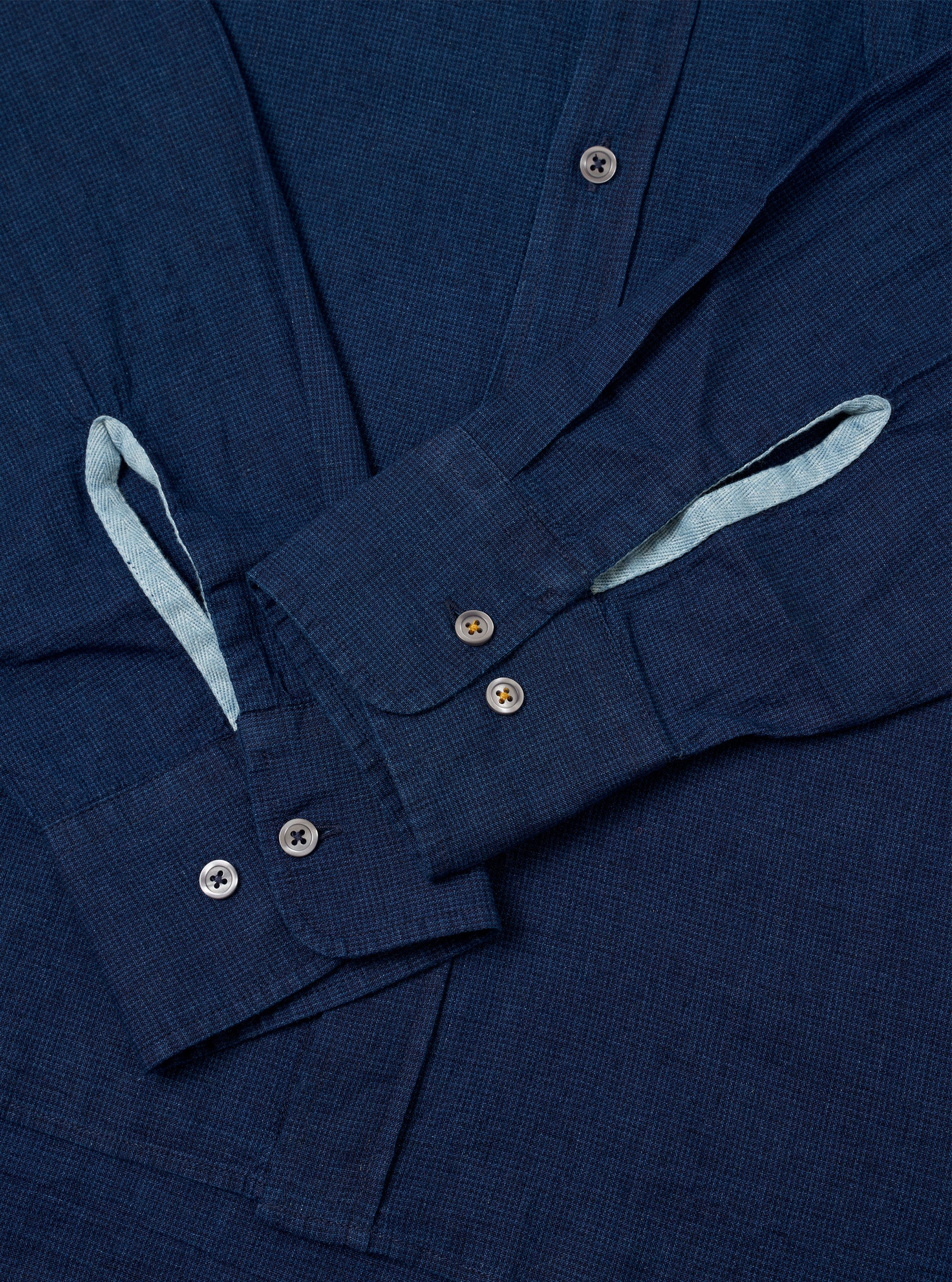 The Indigo Lincot Denim Lazy Day Shirt is shown from the back as a flat lay against a plain white background. The image highlights the back yoke with a central box pleat and the simple, straight-cut hem of the garment. The indigo-colored denim fabric, made from a cotton and linen blend, has a visible, slightly textured weave.